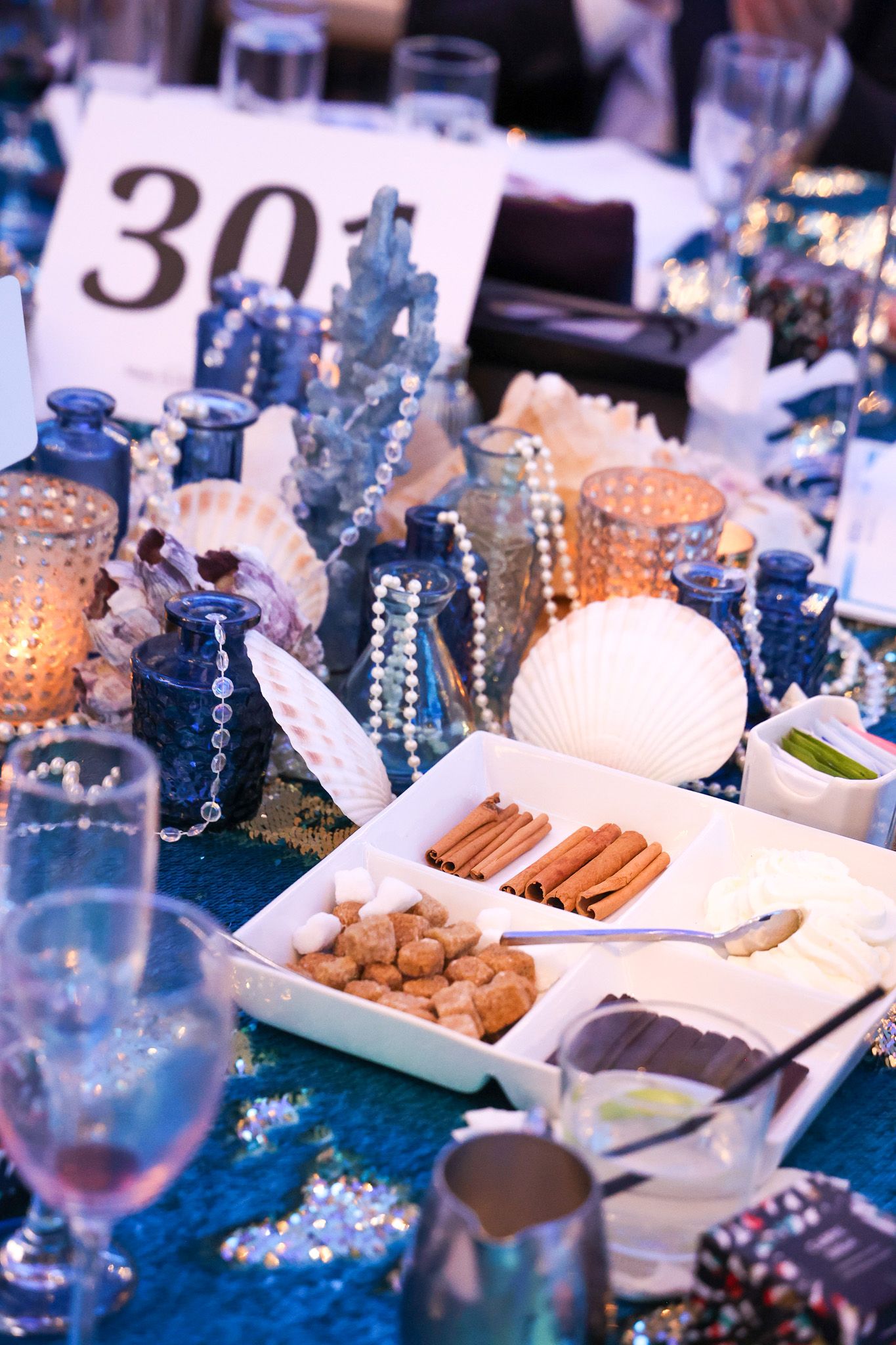 A festive dessert table displays elegant treats, candies, and decorative elements in shades of blue and white.