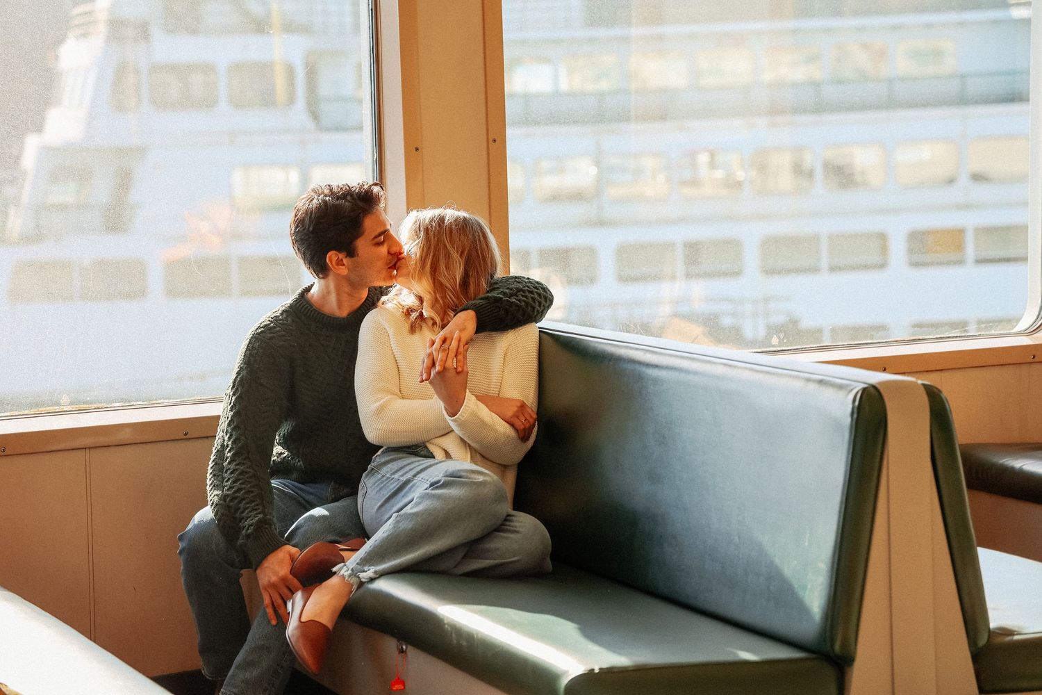 A couple sharing a romantic moment on a ferry bench seat.