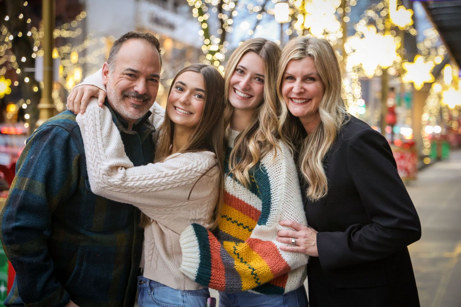 Group of friends sharing warm holiday moments with twinkling lights in background.