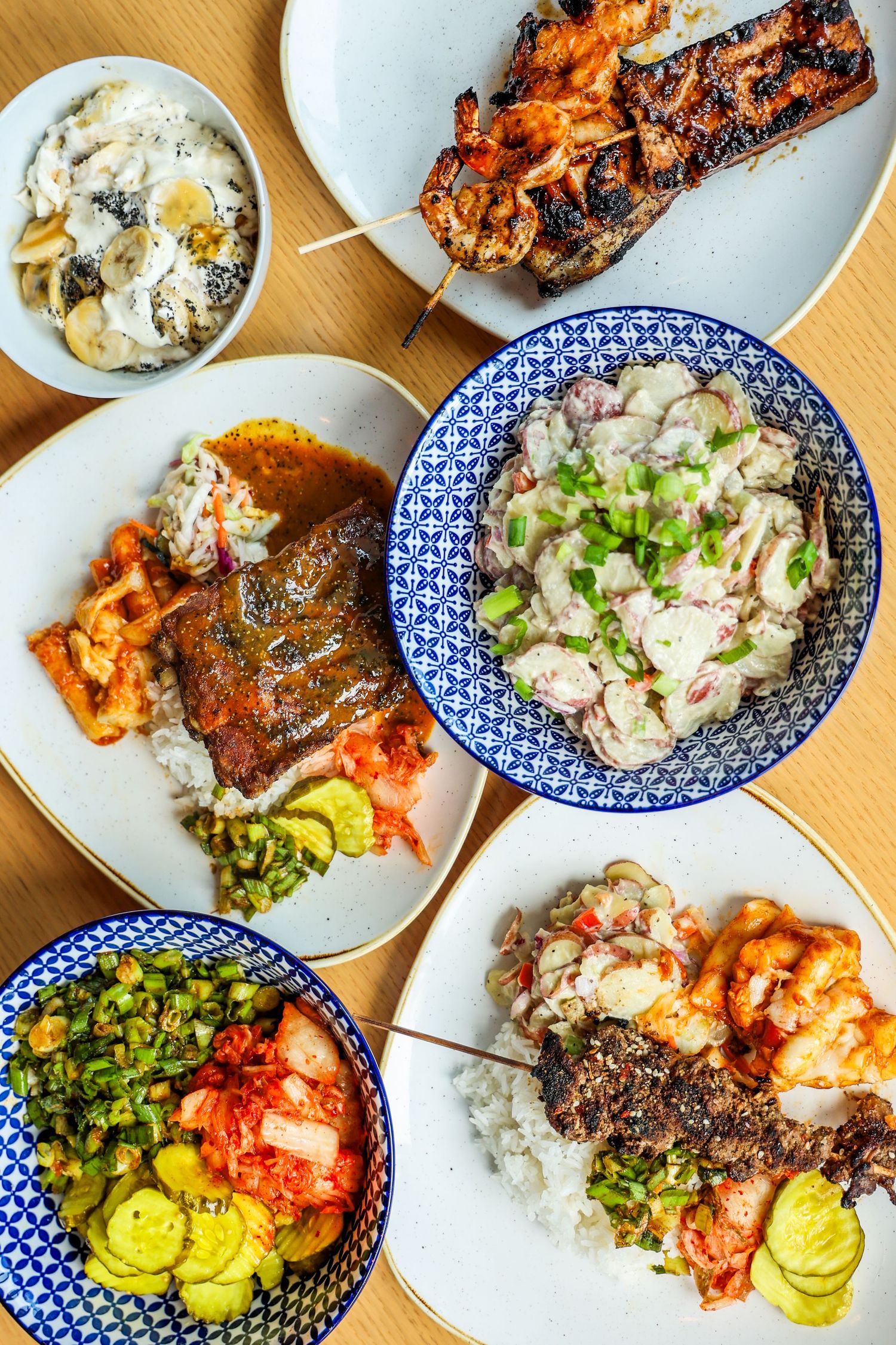Grilled meats and seafood dishes with colorful sides plated on blue and white patterned dishes.