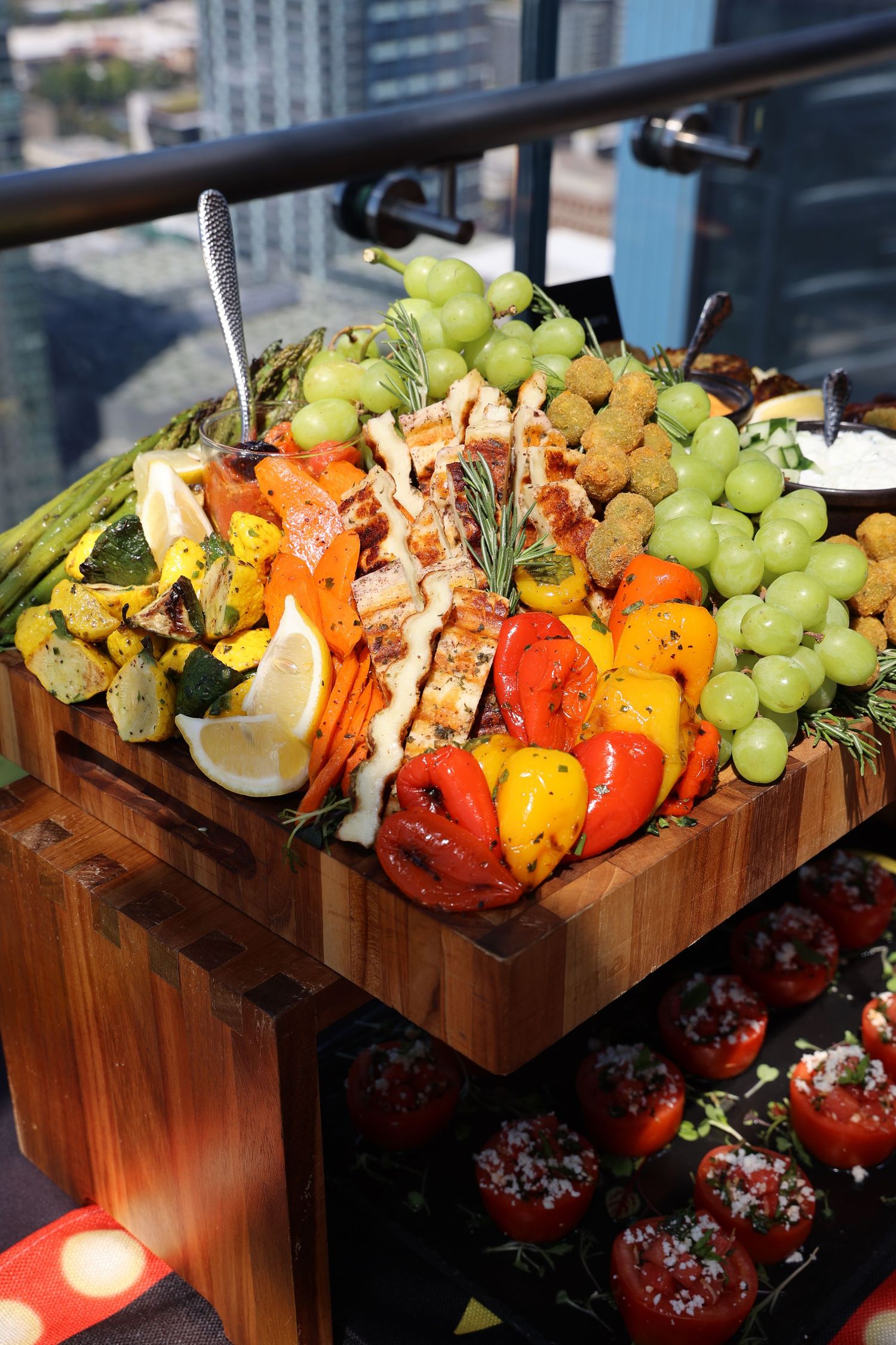 Wooden serving board filled with colorful grilled vegetables, fruits and appetizers.