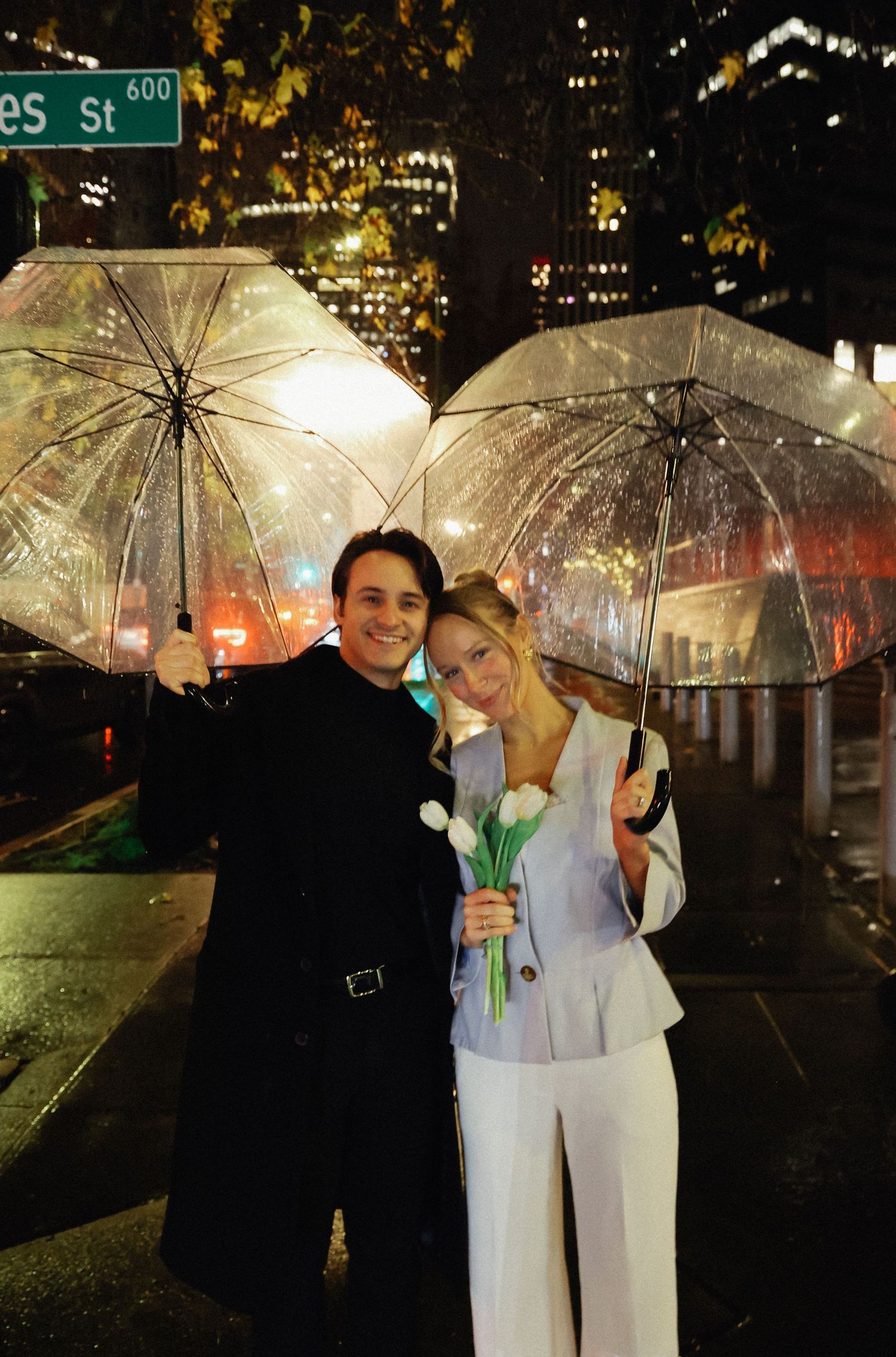 A couple shares romantic moments under clear umbrellas at night on a city street.