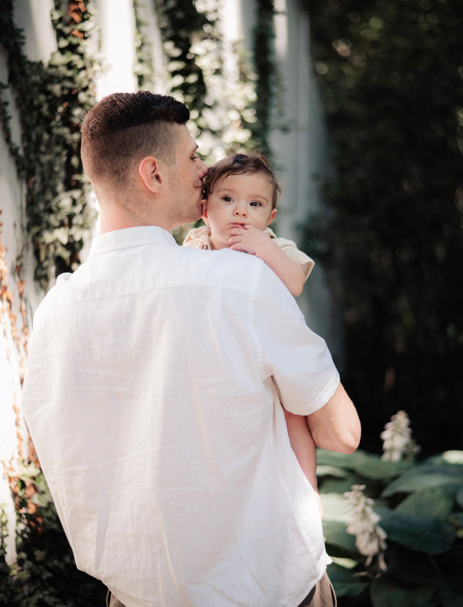 Tender parenting moment captured against white pillars in garden setting.