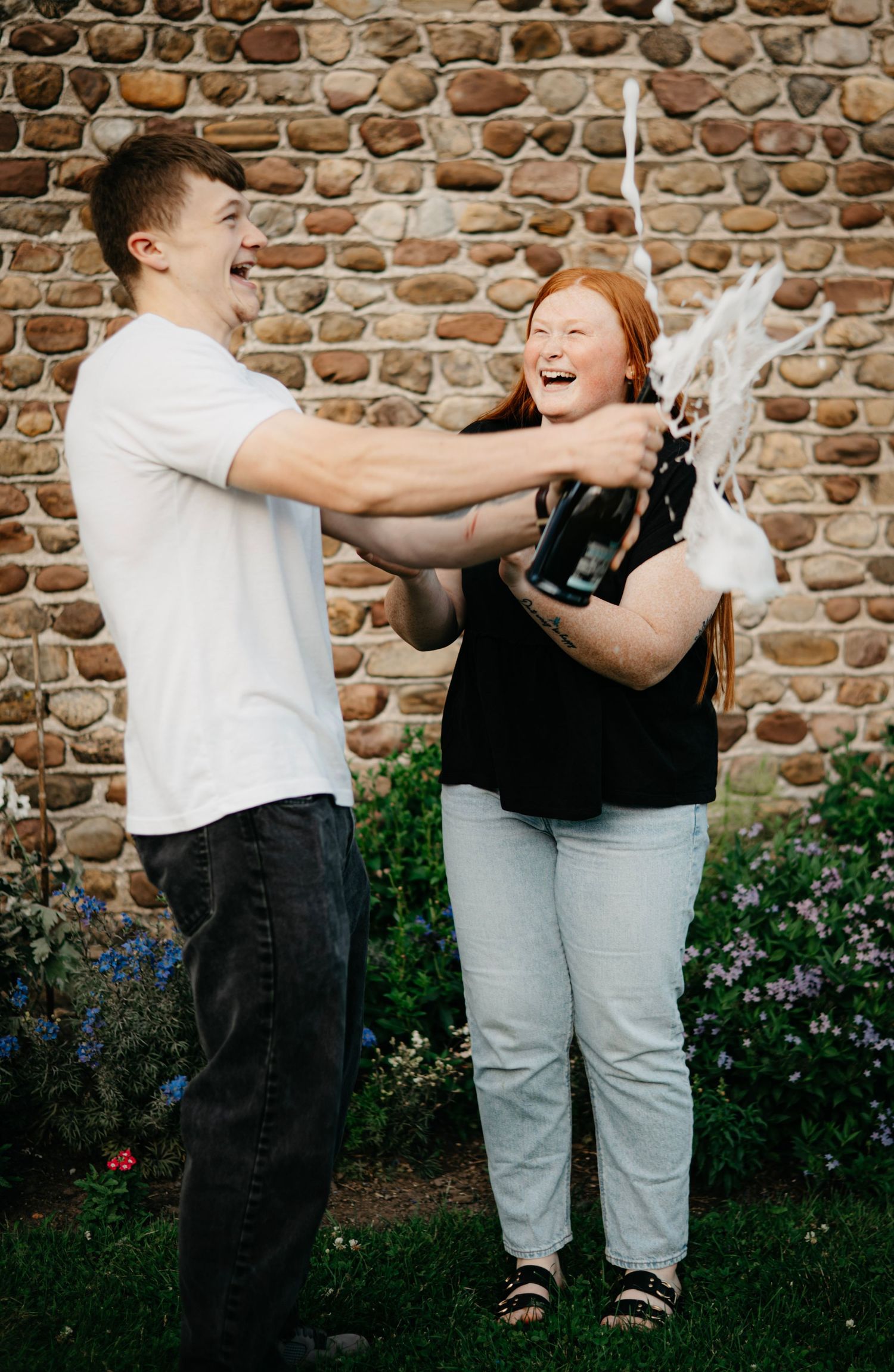 Couple celebrating with champagne against a brick wall backdrop.
