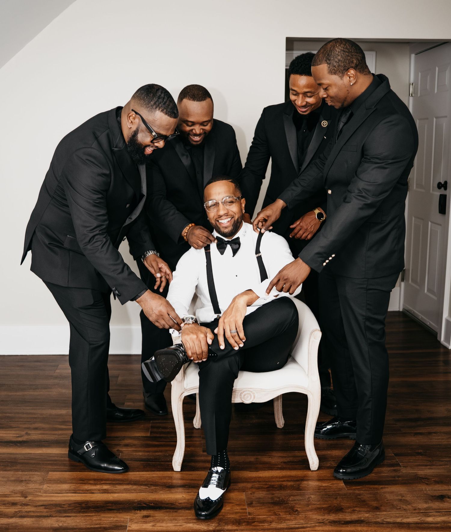 A group of men in black suits gather around a child in a white suit sitting in a chair for a formal portrait.