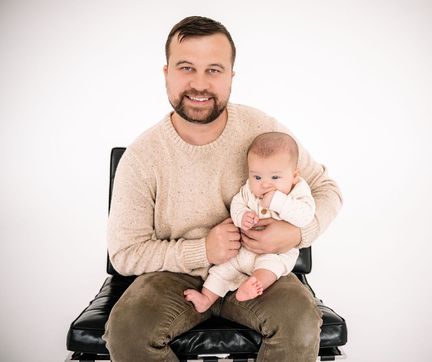 A series of four photos showing an adult in a beige sweater holding a small baby in a white onesie on a chair.
