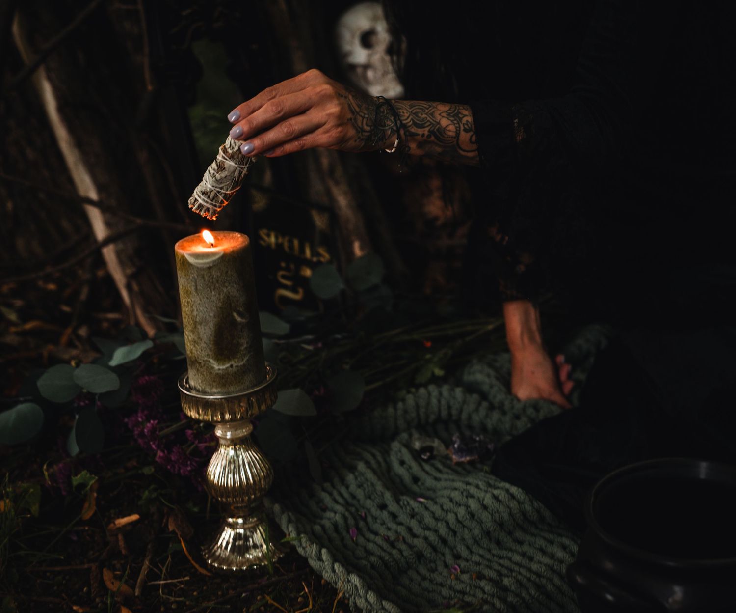 Atmospheric still life of burning candles and greenery arranged on a dark surface with moody lighting.