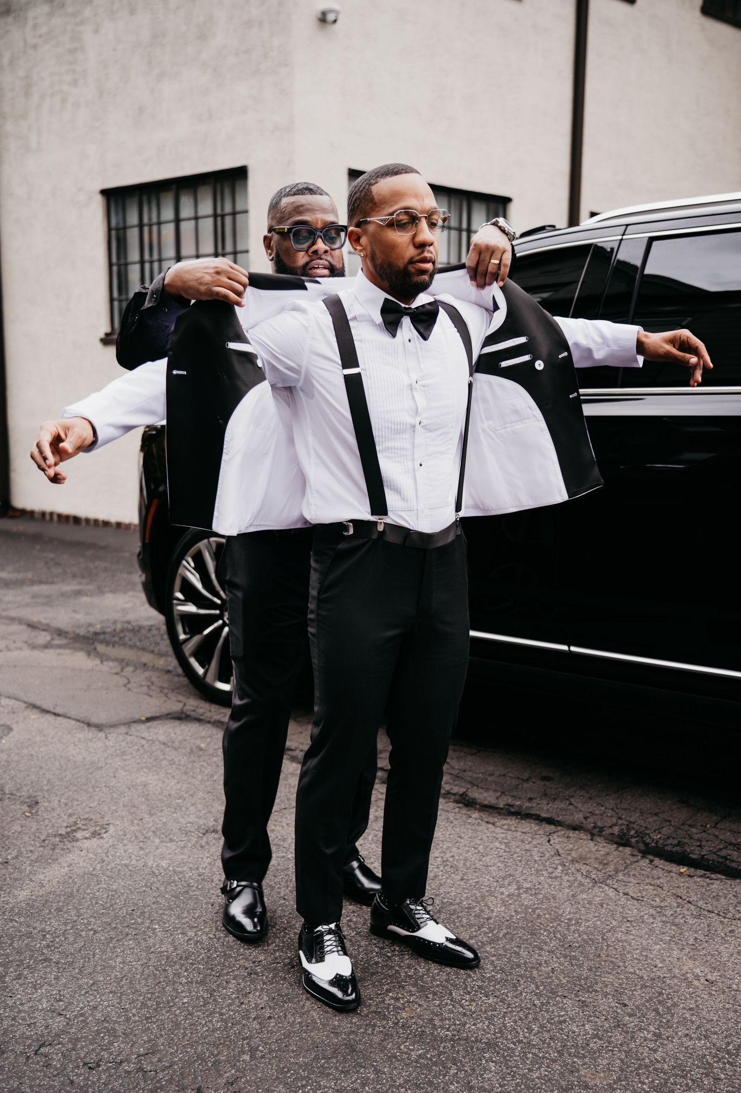 Formal event attendees in black and white attire gathered near luxury vehicle outdoors.