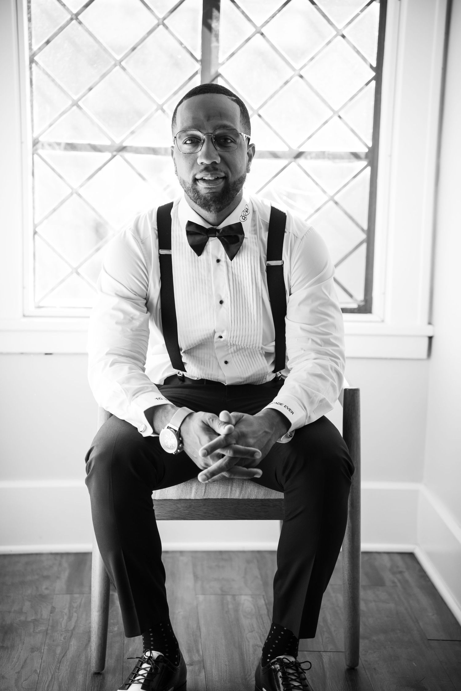 Formal attire with black bow tie and suspenders sitting in bright room with hardwood floors and white walls.