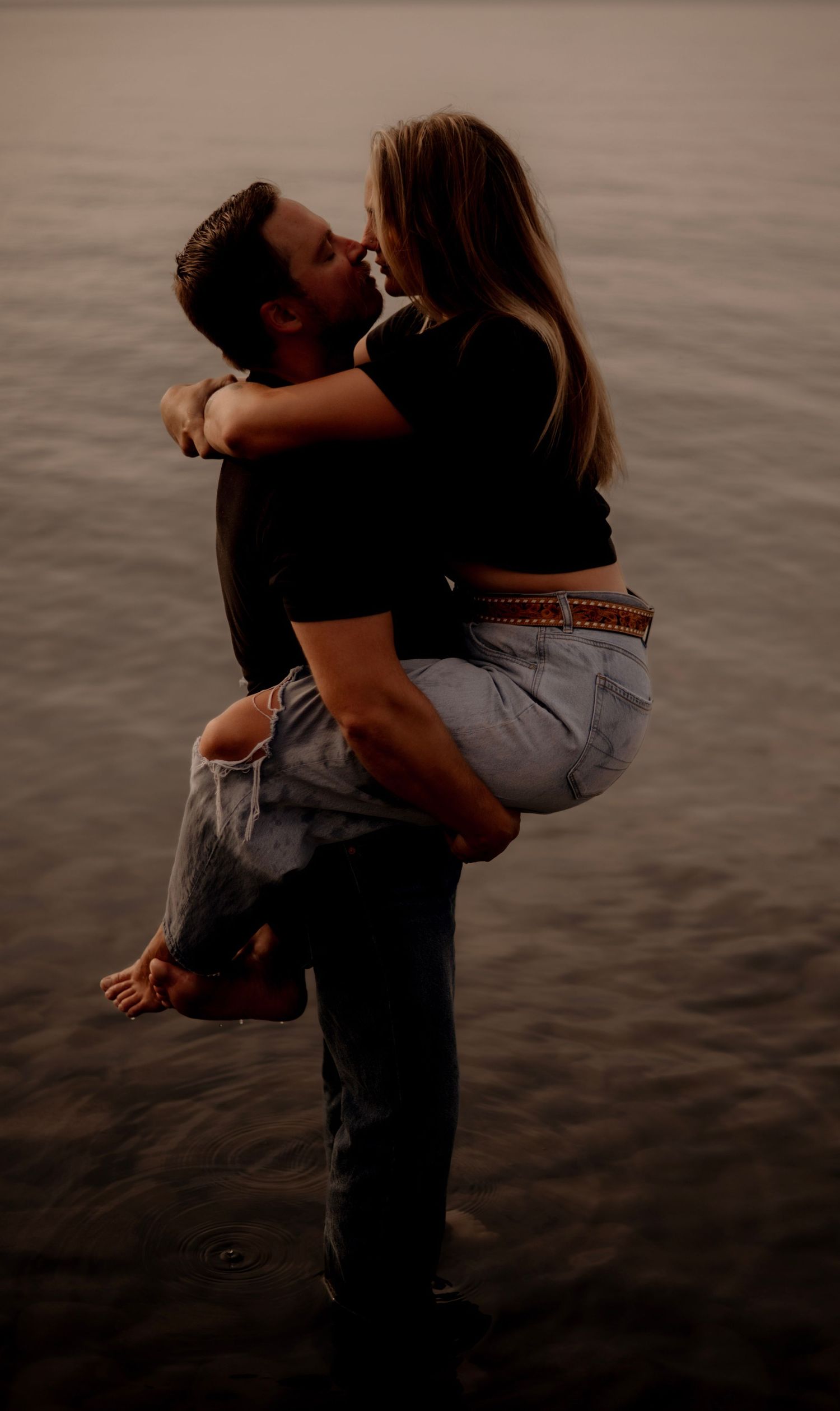 Two people share an intimate embrace near water at dusk in a series of romantic silhouetted photos.