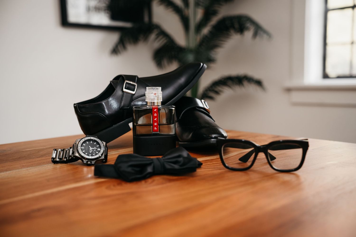 A collection of men's accessories including black dress shoes, sunglasses, watch and cologne on a wooden table.