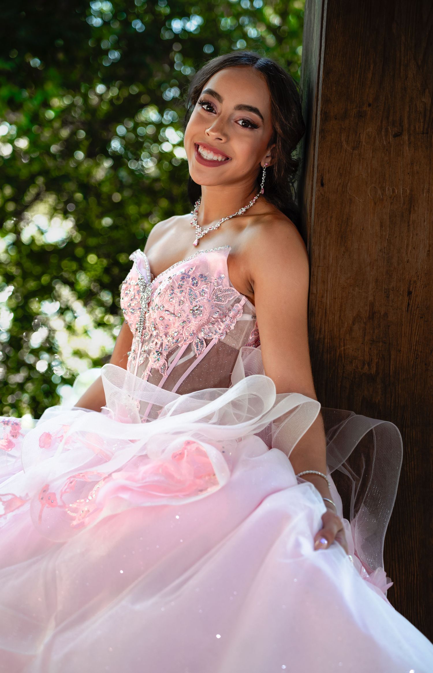A quinceañera celebration featuring a flowing pink and white ball gown with delicate lace details in an outdoor setting.