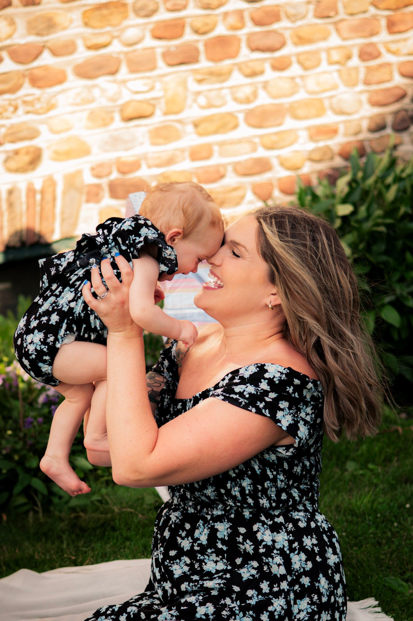 A sweet bonding moment outdoors against a brick wall in a floral dress.
