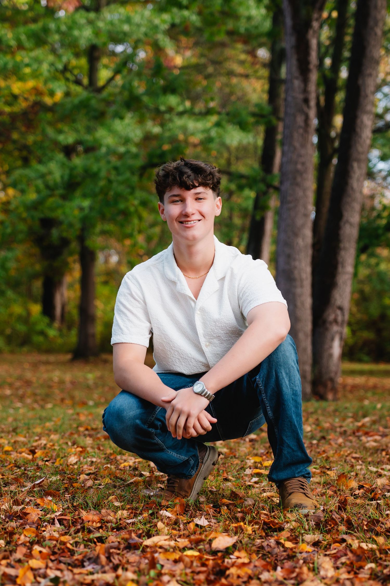 Autumn portrait series sitting among fallen leaves in a wooded park setting wearing casual attire.