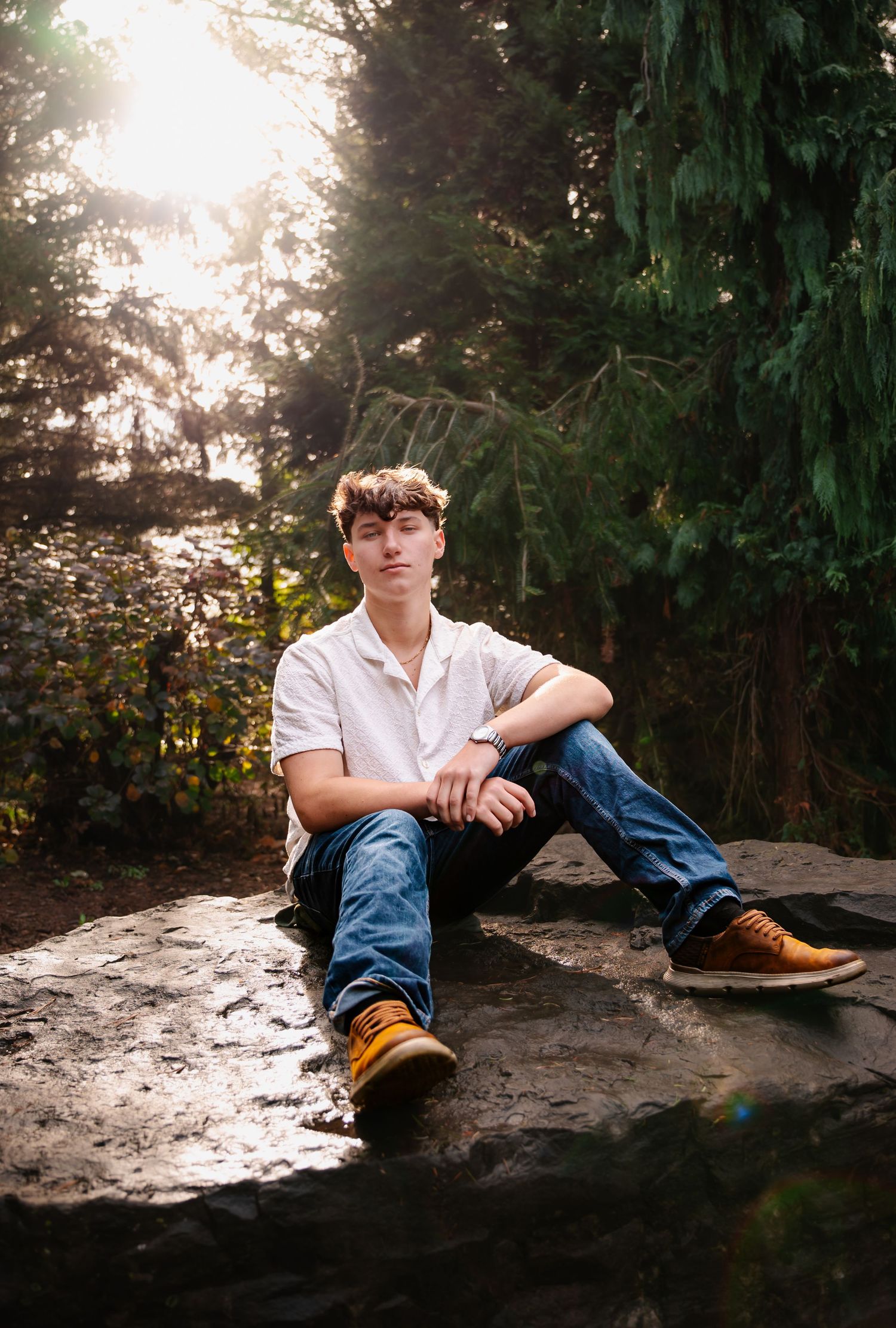 Artistic sunset portrait on a rock with evergreen trees and golden sunlight filtering through the forest.