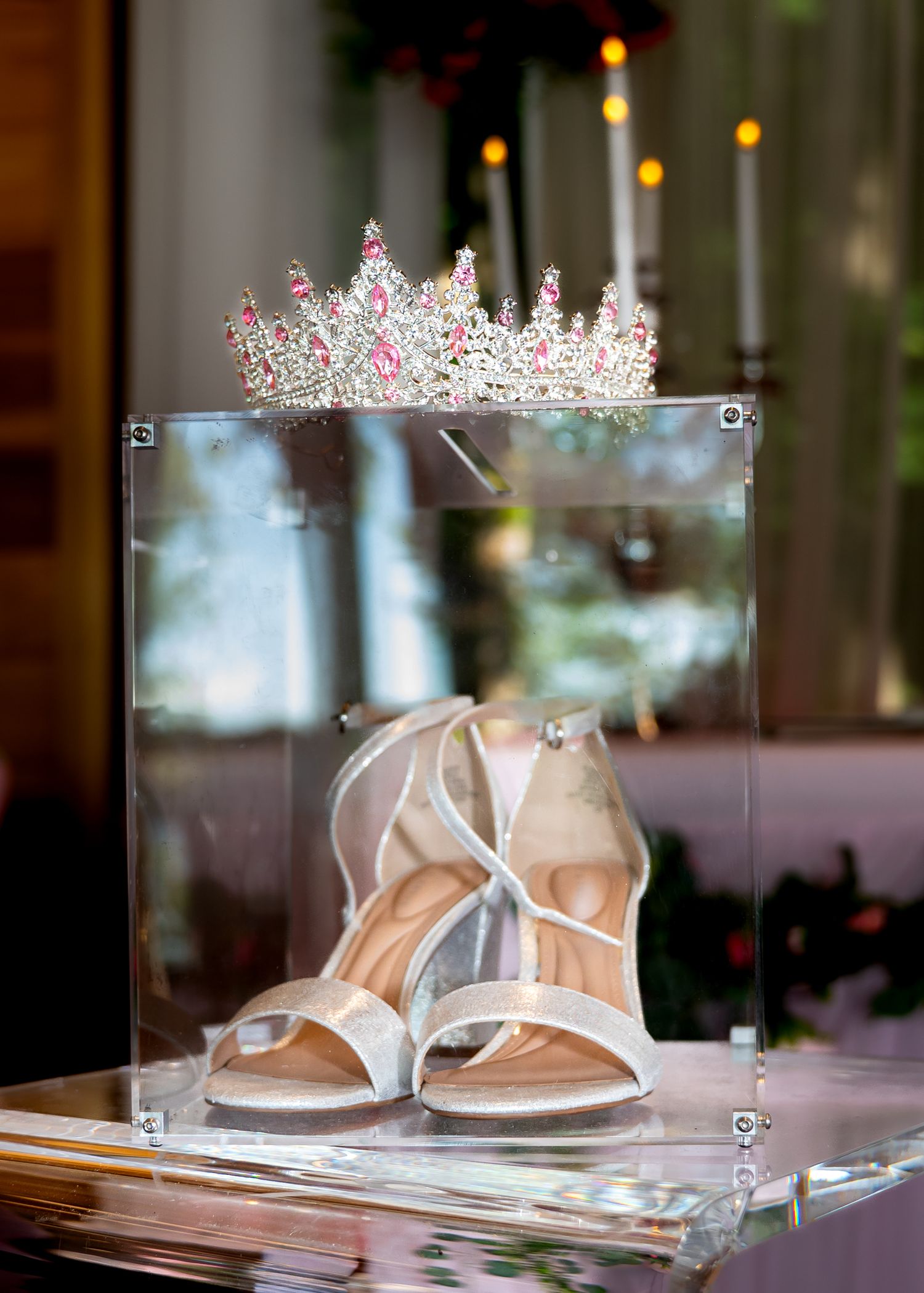 Wedding accessories including delicate tiaras and elegant white heels displayed on a glass table with soft lighting.