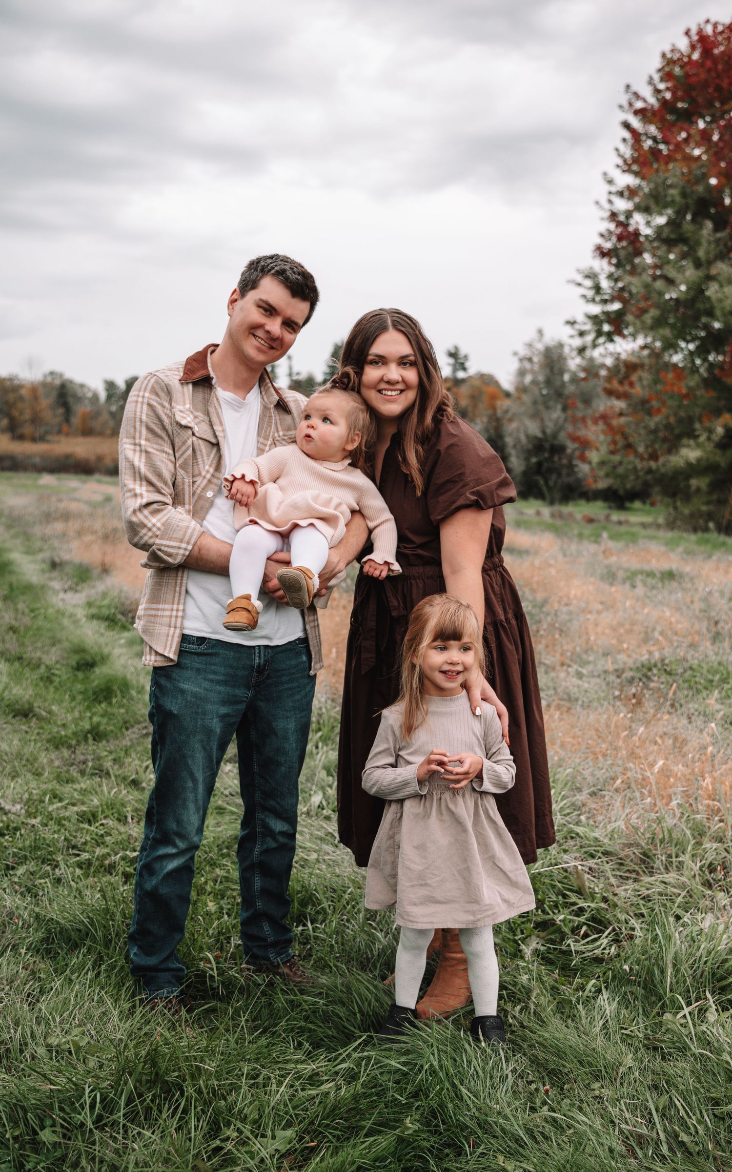 A family shares tender moments together in a field with autumn foliage during an outdoor photo session.