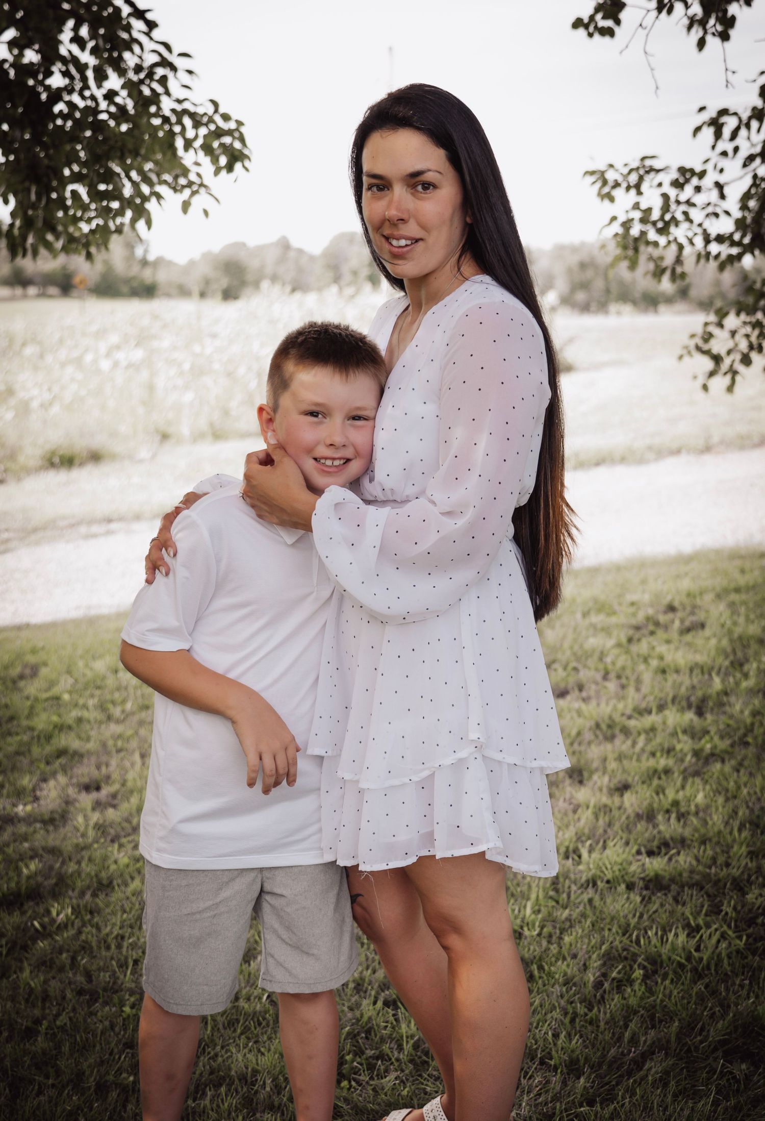 An outdoor family portrait against a natural landscape with trees and grass.