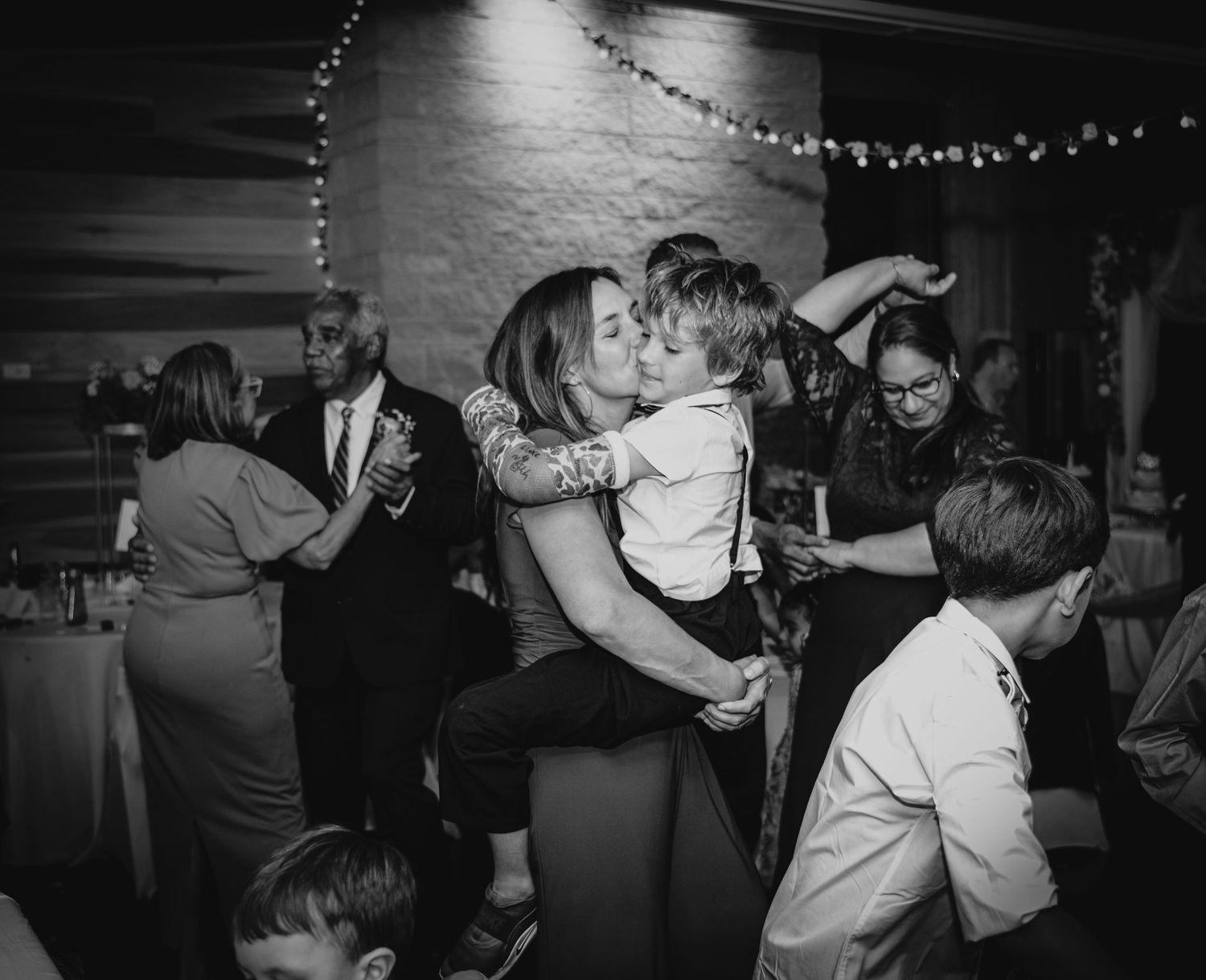 Black and white photos show couples dancing and embracing at a dimly lit party with string lights overhead.