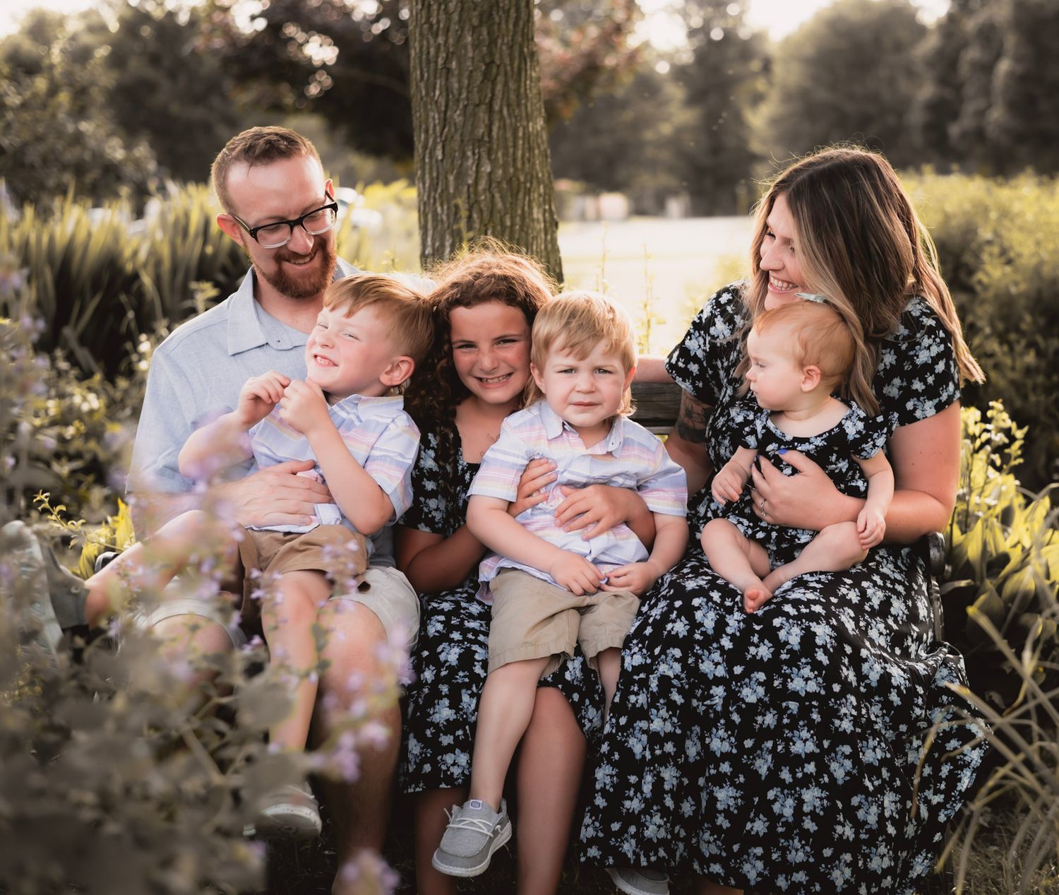 A family photo session in a sunlit outdoor setting with playful interactions and natural laughter.