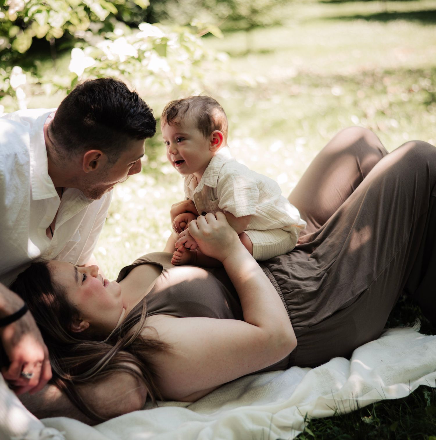A tender moment between parent and newborn baby captured in soft natural lighting during an outdoor photography session.