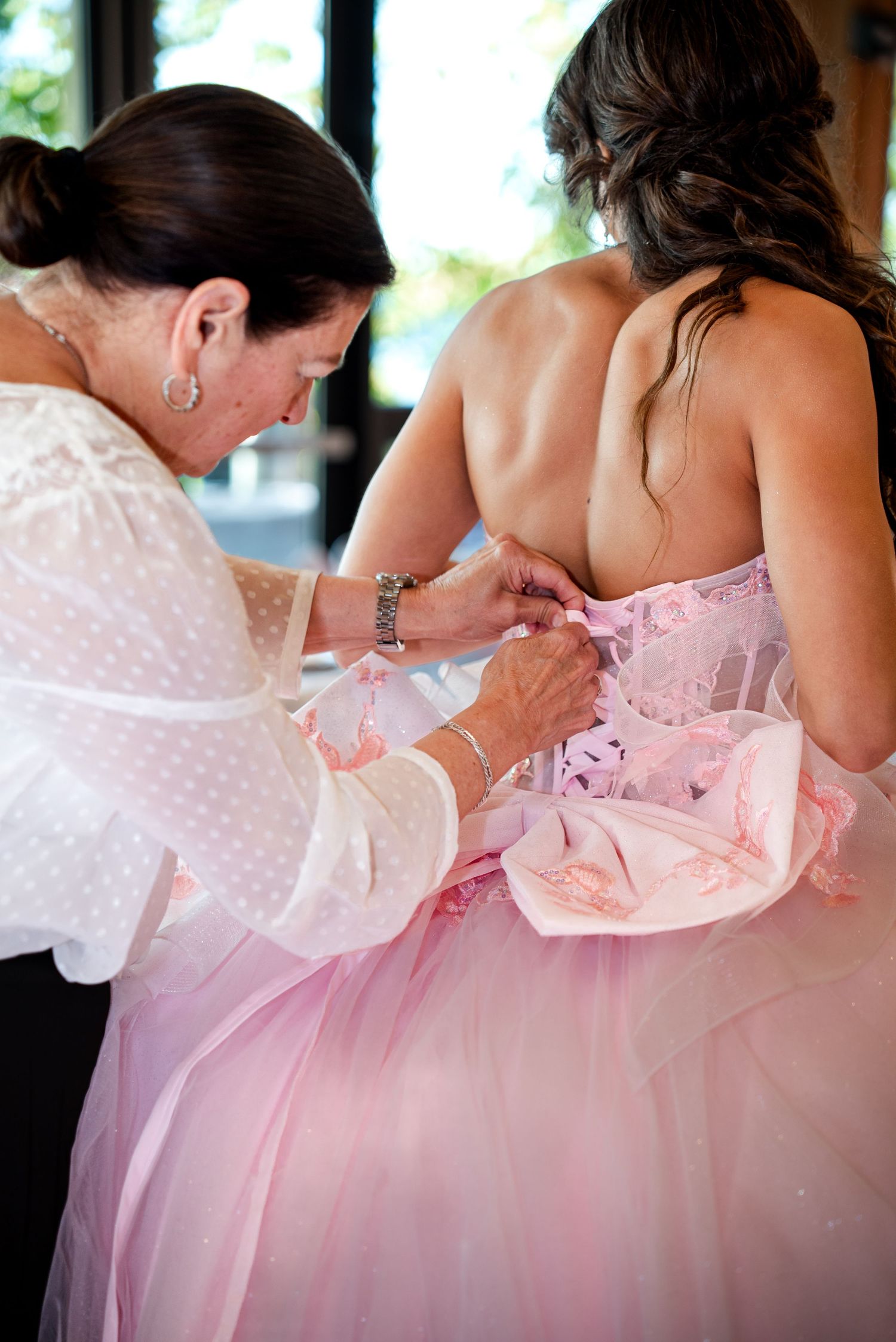 Someone helps adjust the lacing on a pink ball gown during a formal dress fitting.