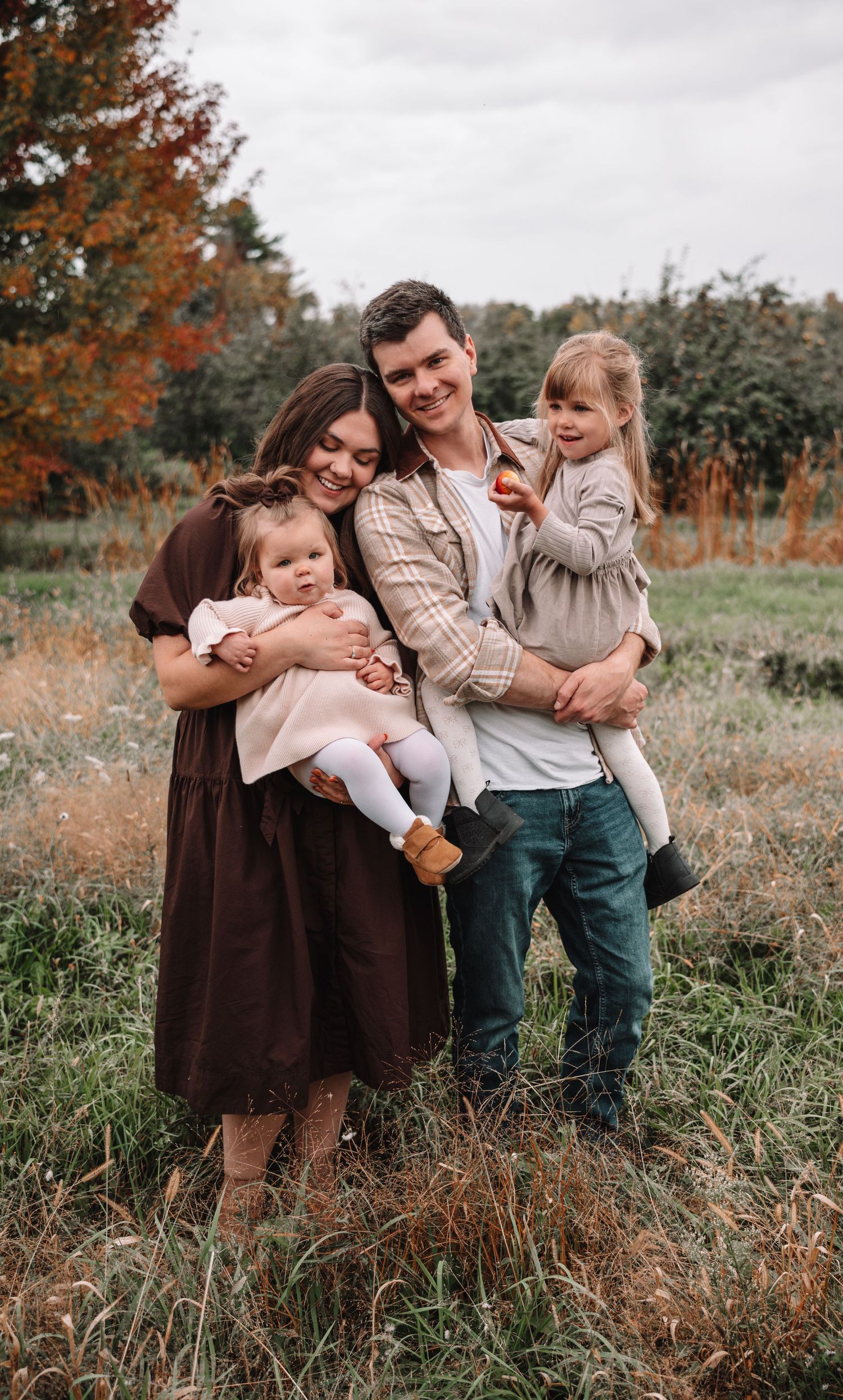 A family shares joyful moments together in a field with autumn foliage in the background.