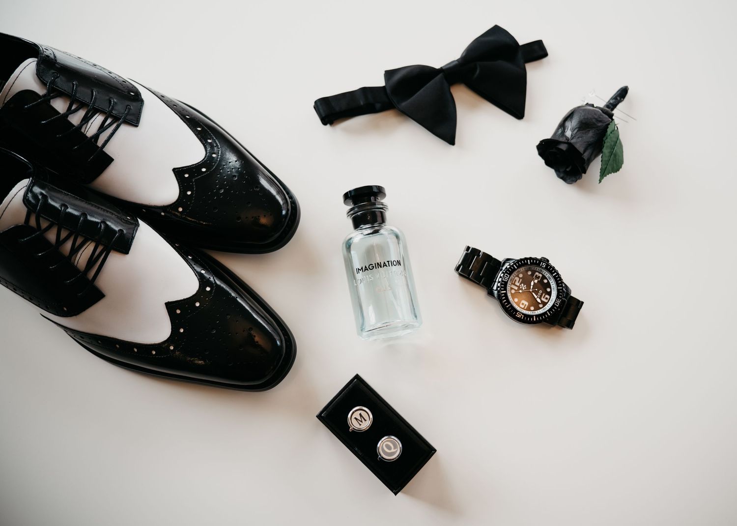 A collection of black shoes and accessories including bow ties and bottles arranged on a white background.