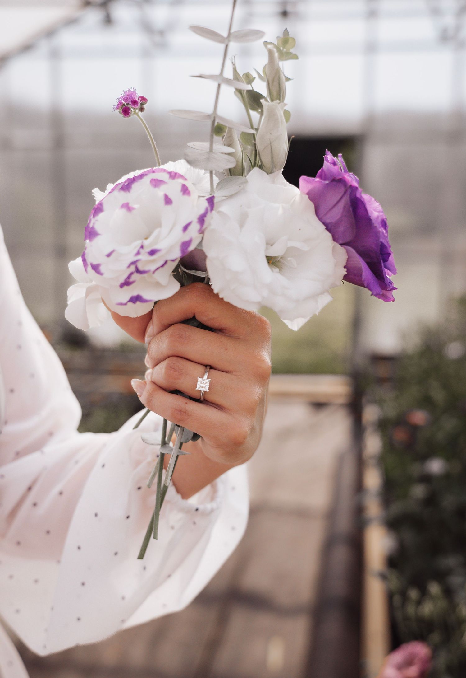 A delicate hand holding purple and white flowers against a blurred background.