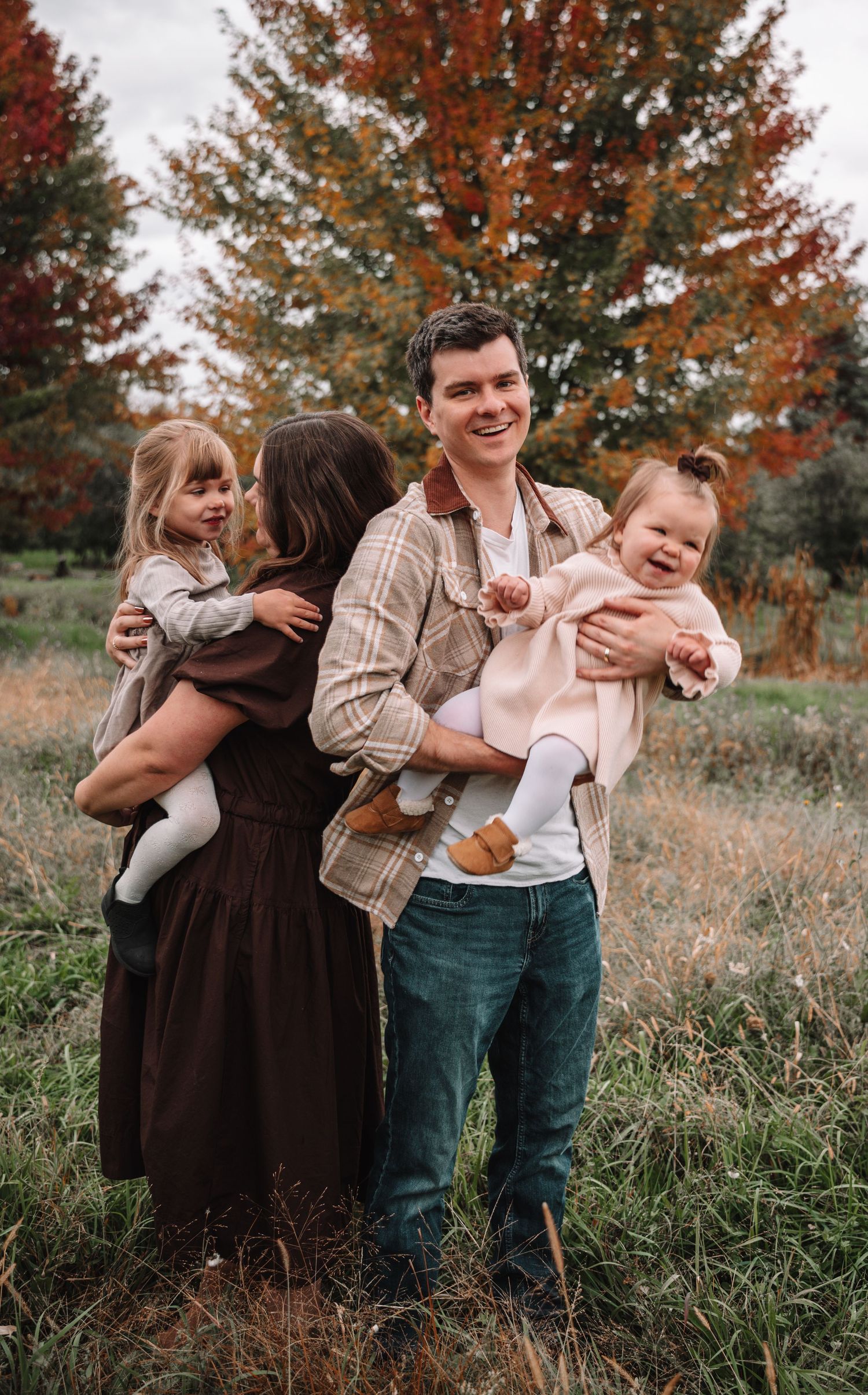 A family shares joyful moments together in a field during autumn with vibrant orange trees in the background.