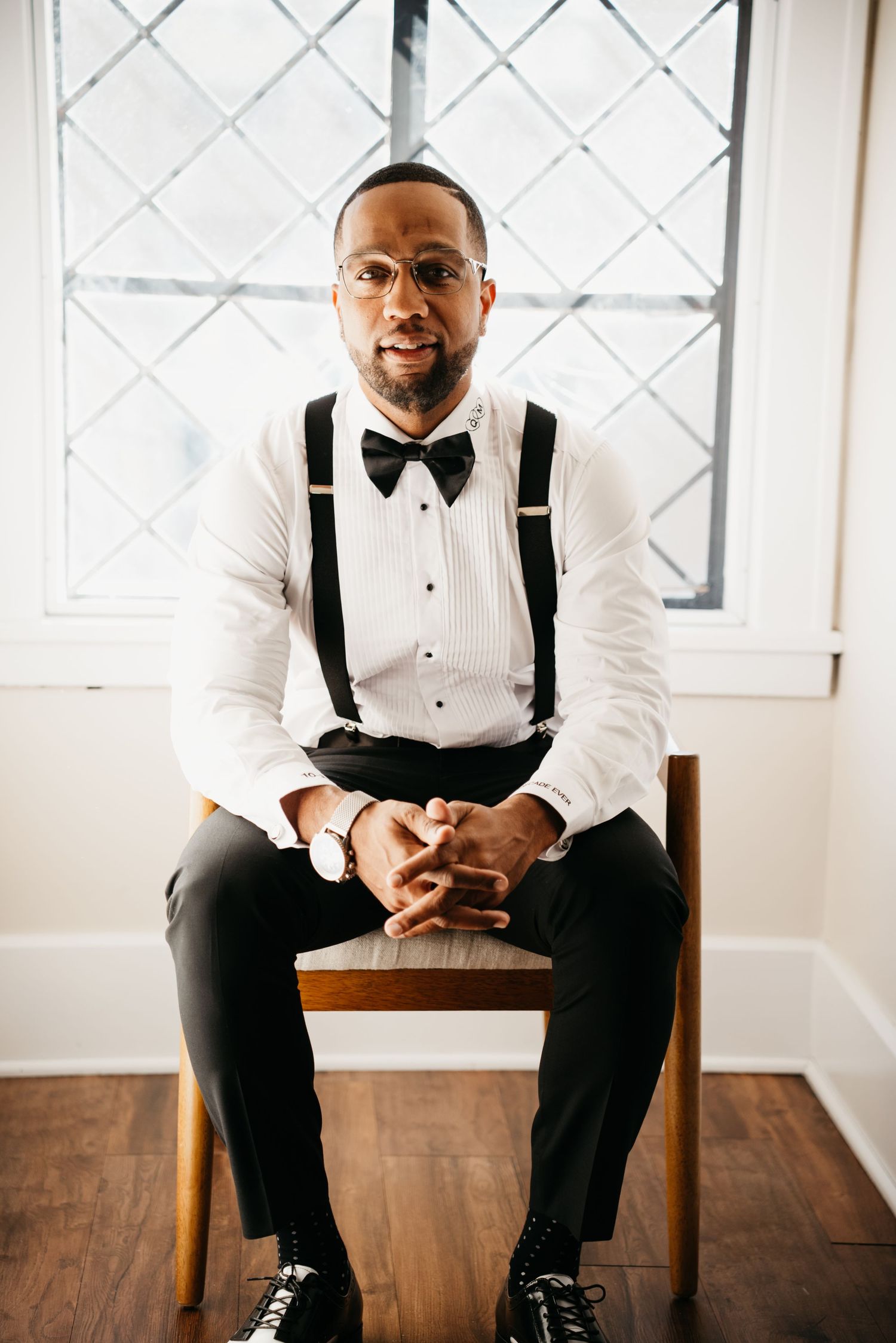 Formal attire with black bow tie and suspenders sitting in bright room with hardwood floors and white walls.