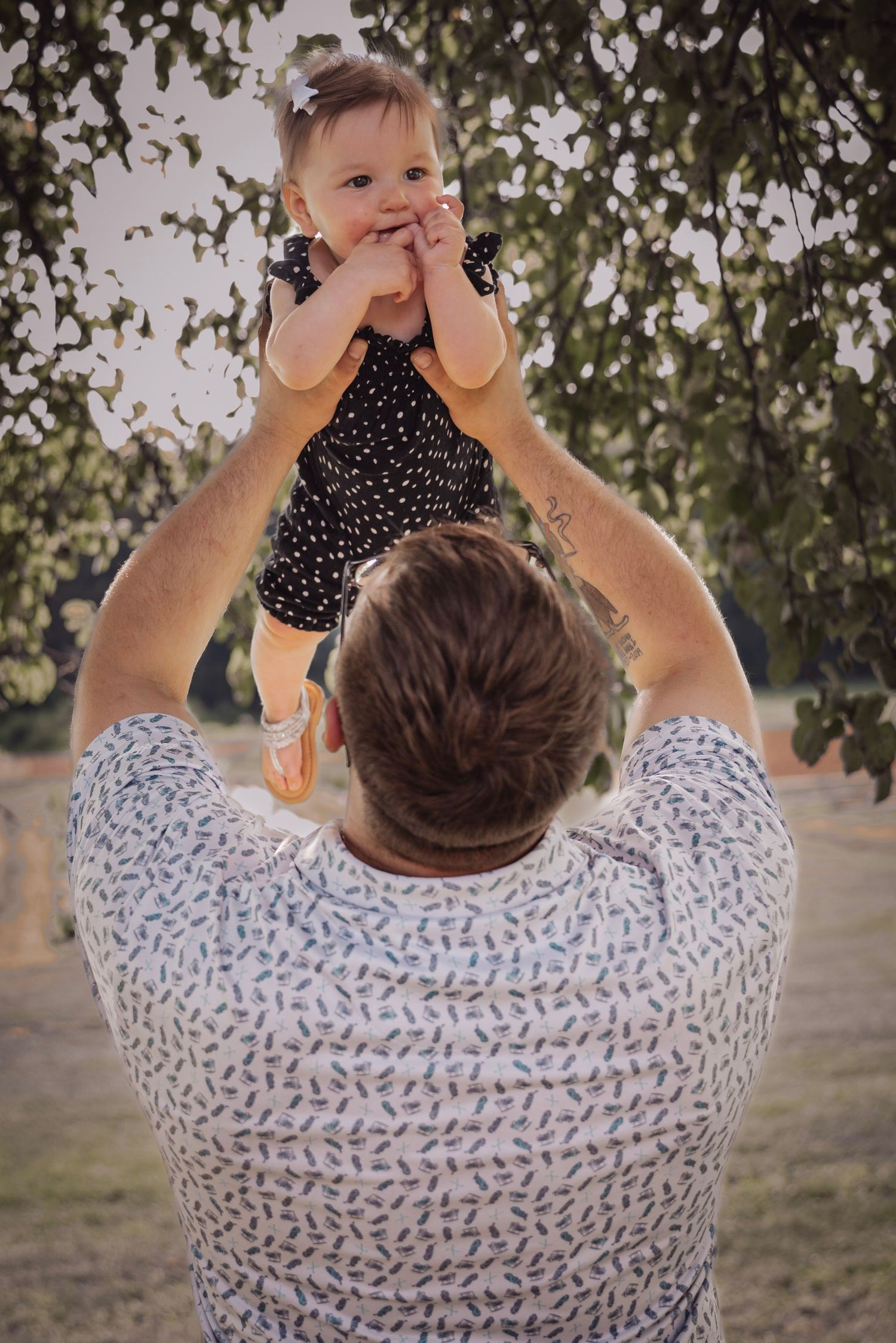A playful moment of parental bonding outdoors with a baby wearing a polka dot outfit.