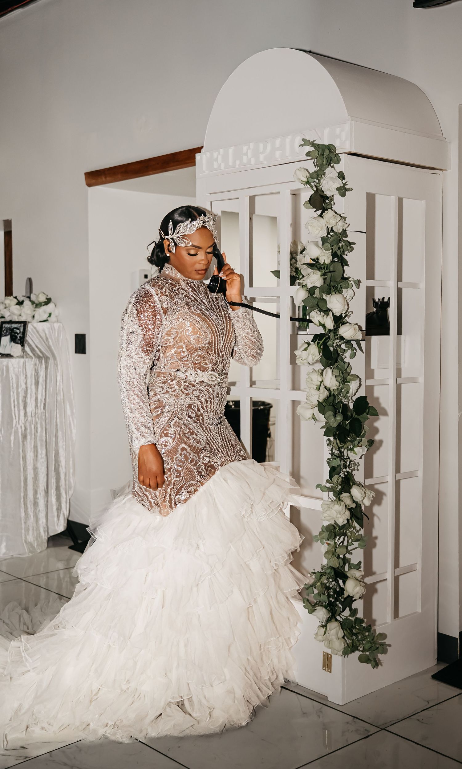 A bridal gown with intricate lace details and voluminous tulle skirt is displayed in a white room with ivy decorations.