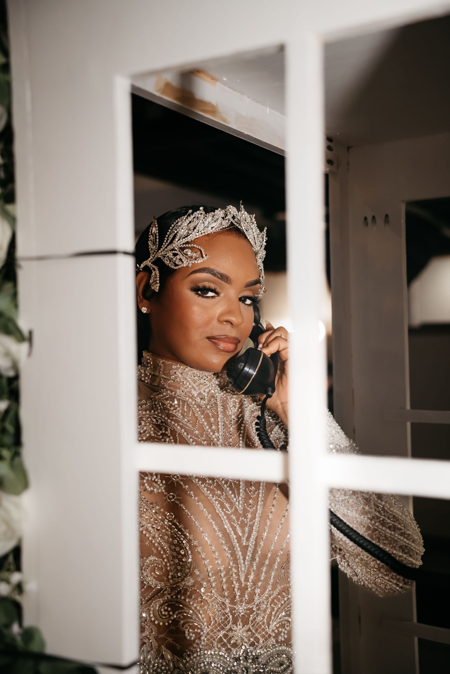 A glamorous bridal portrait through window panes showing sparkly dress and crystal headpiece.