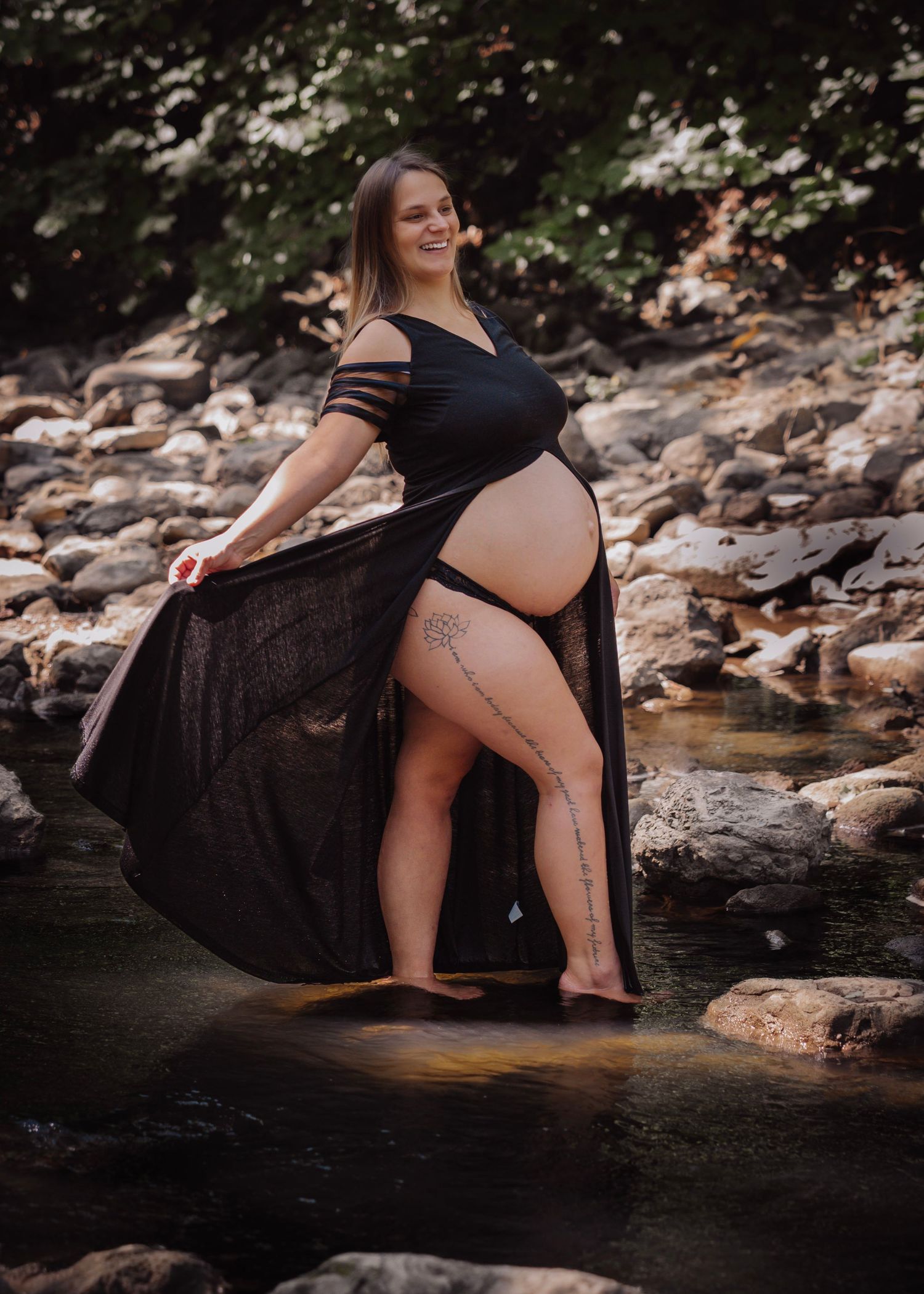 Pregnant woman in flowing dress in sunlit water with boho vibe