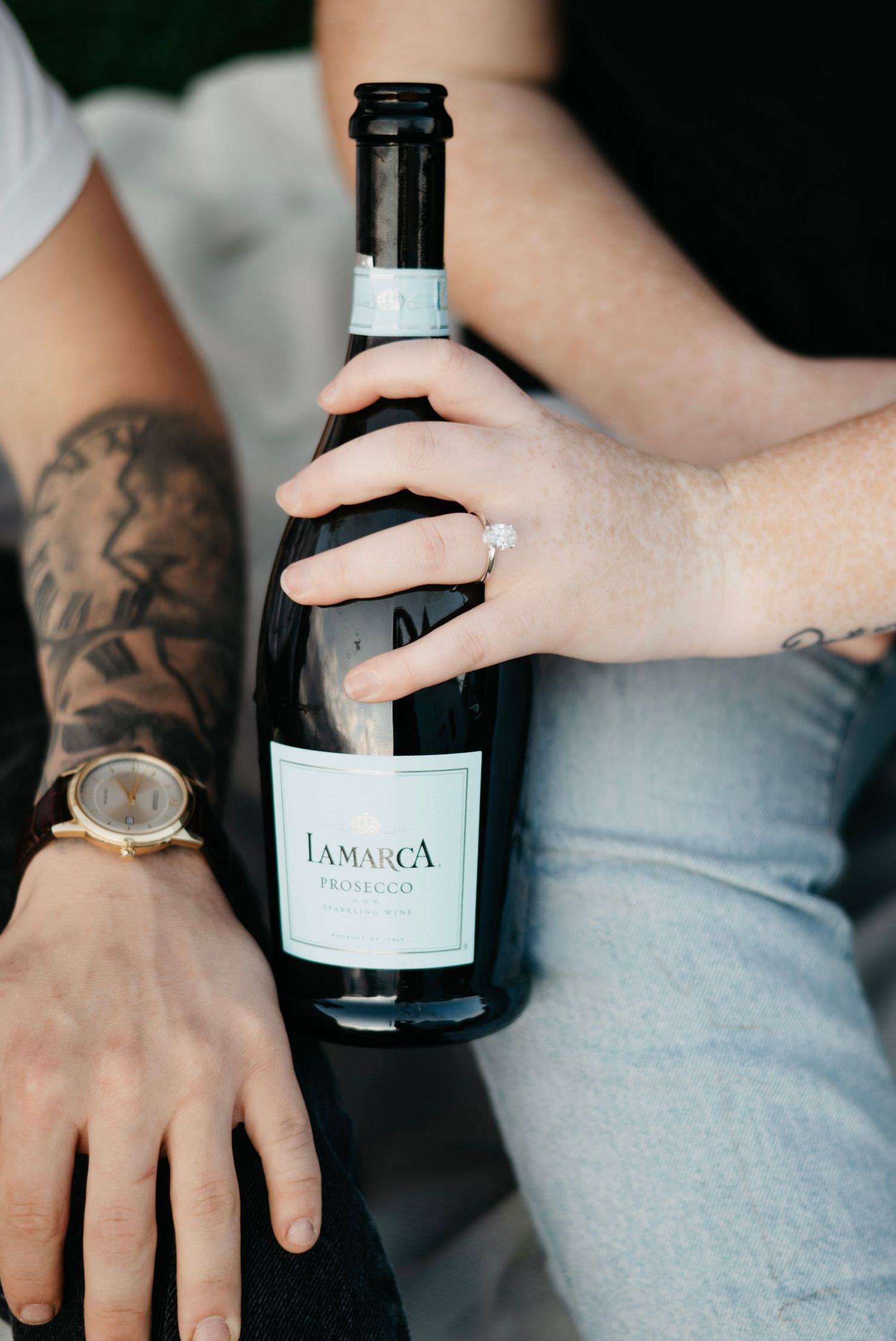 Close-up series showing tattooed hands holding a bottle of wine against a light gray background.