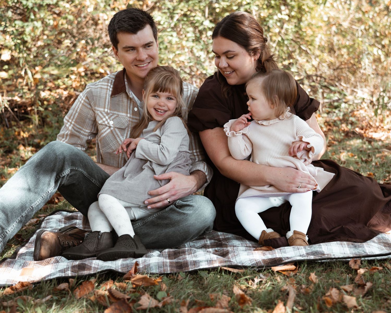 Family relaxes together on autumn leaves in a park during a casual outdoor photo session.