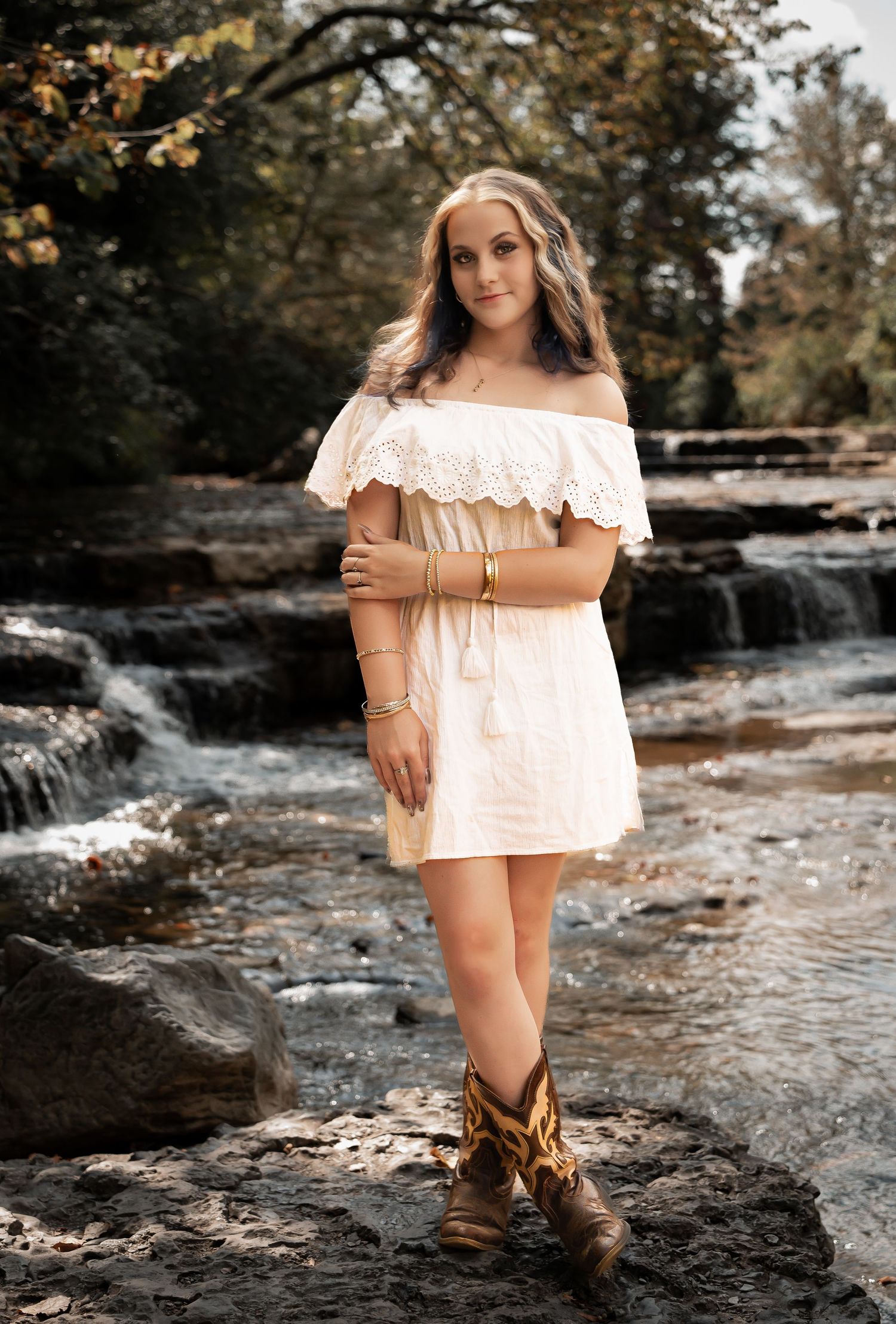 A series of outdoor portrait photographs taken at a scenic waterfall location with rustic brown boots and cream dress.