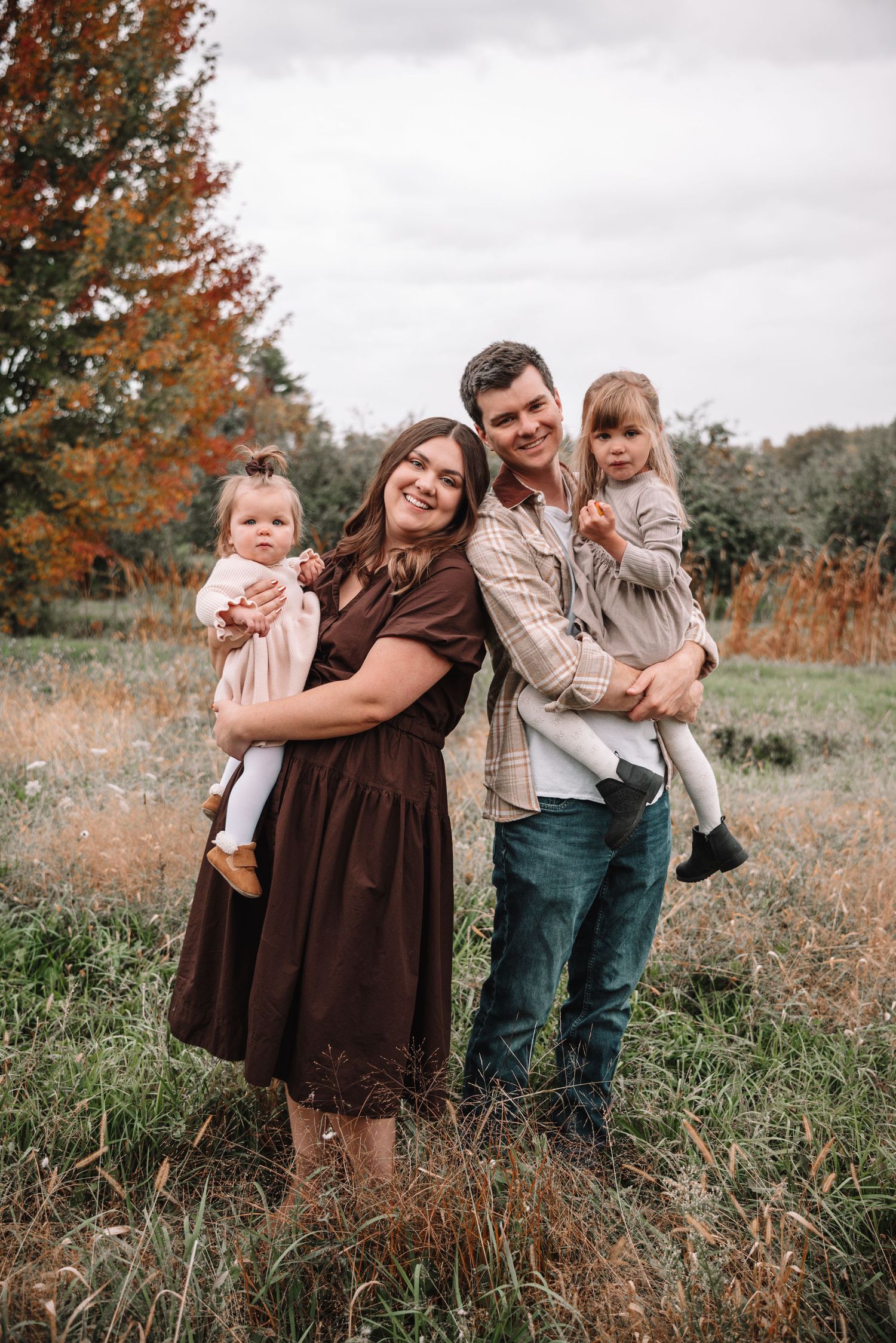 A family stands together in a field with autumn foliage and grass during a fall photo session.