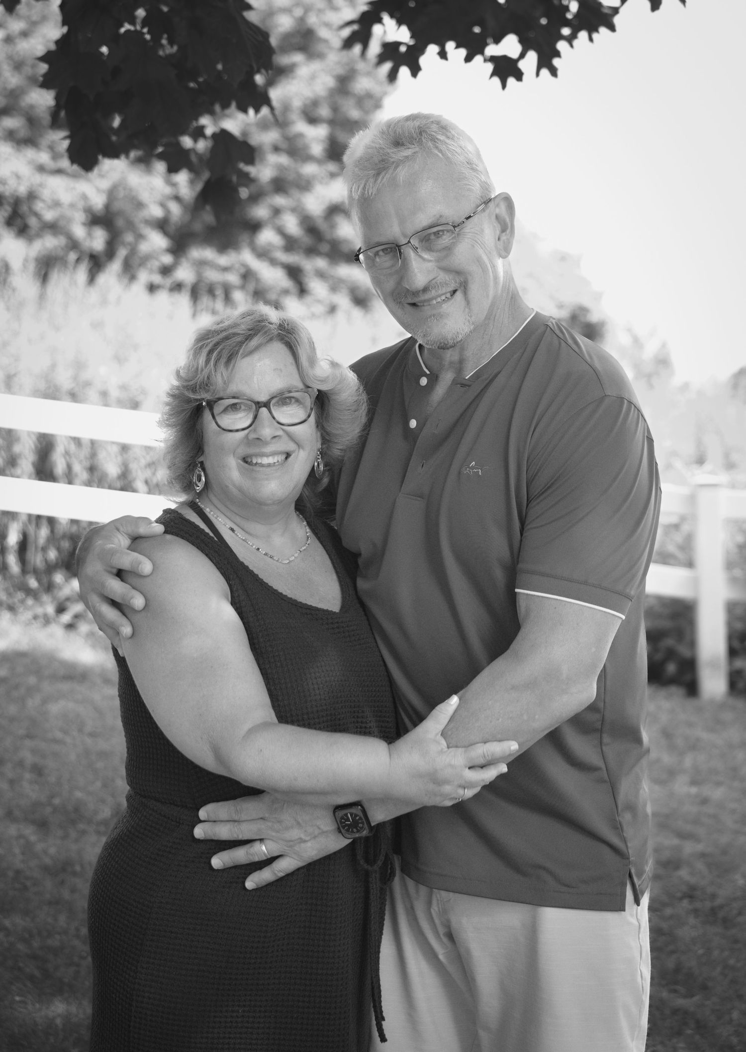 Black and white portrait of a happy mature couple embracing outdoors by a white fence on a sunny day.