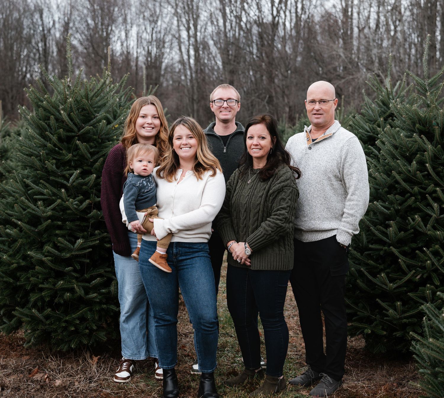 A group stands together among evergreen trees at a Christmas tree farm on a winter day.