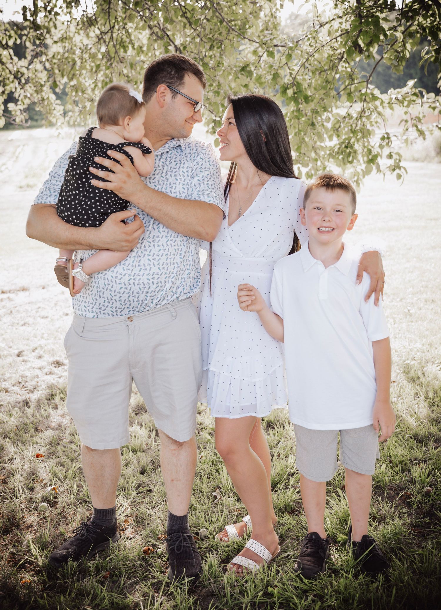 Family of four smiling and holding hands in forest setting