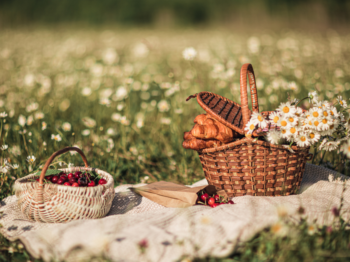 Two woven picnic baskets sit on a blanket in a daisy-filled meadow on a sunny summer day.