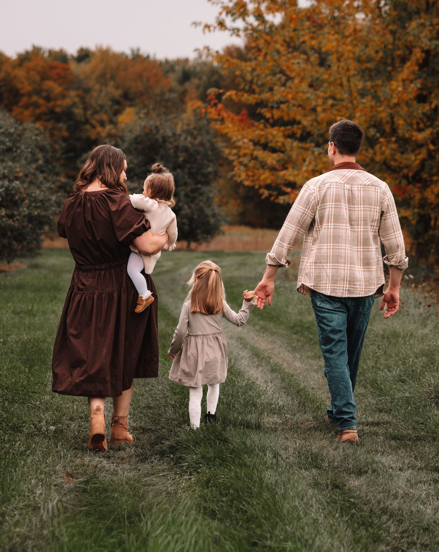A group walks down a grassy path surrounded by autumn trees with golden foliage in the background.
