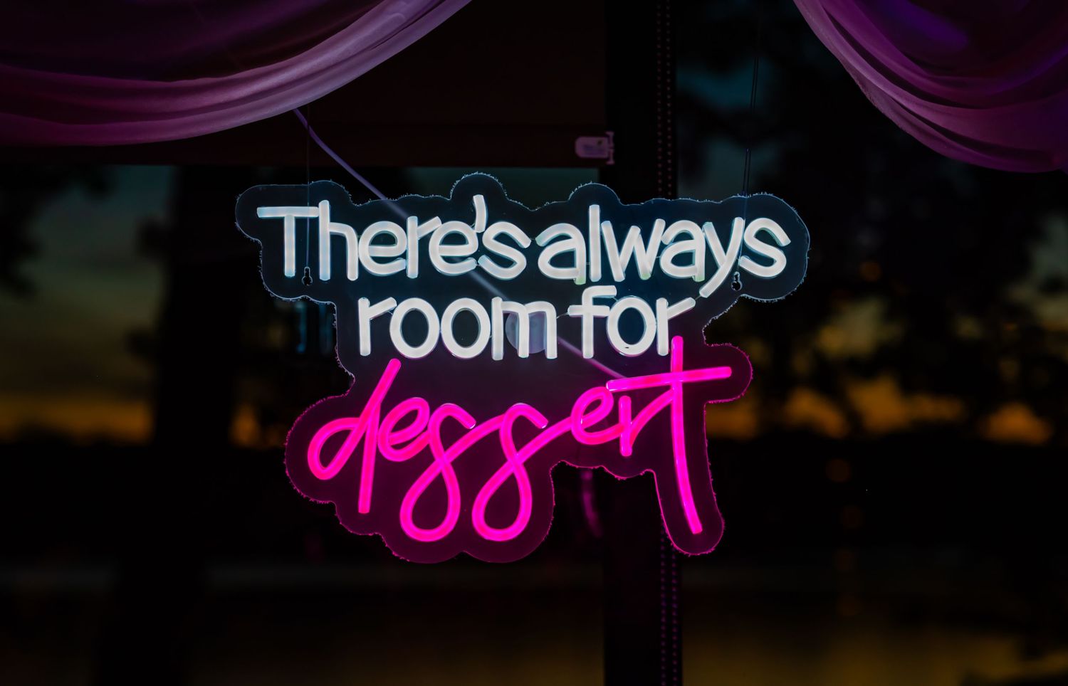 Purple neon sign displays 'There's always room for dessert' against a dark background.