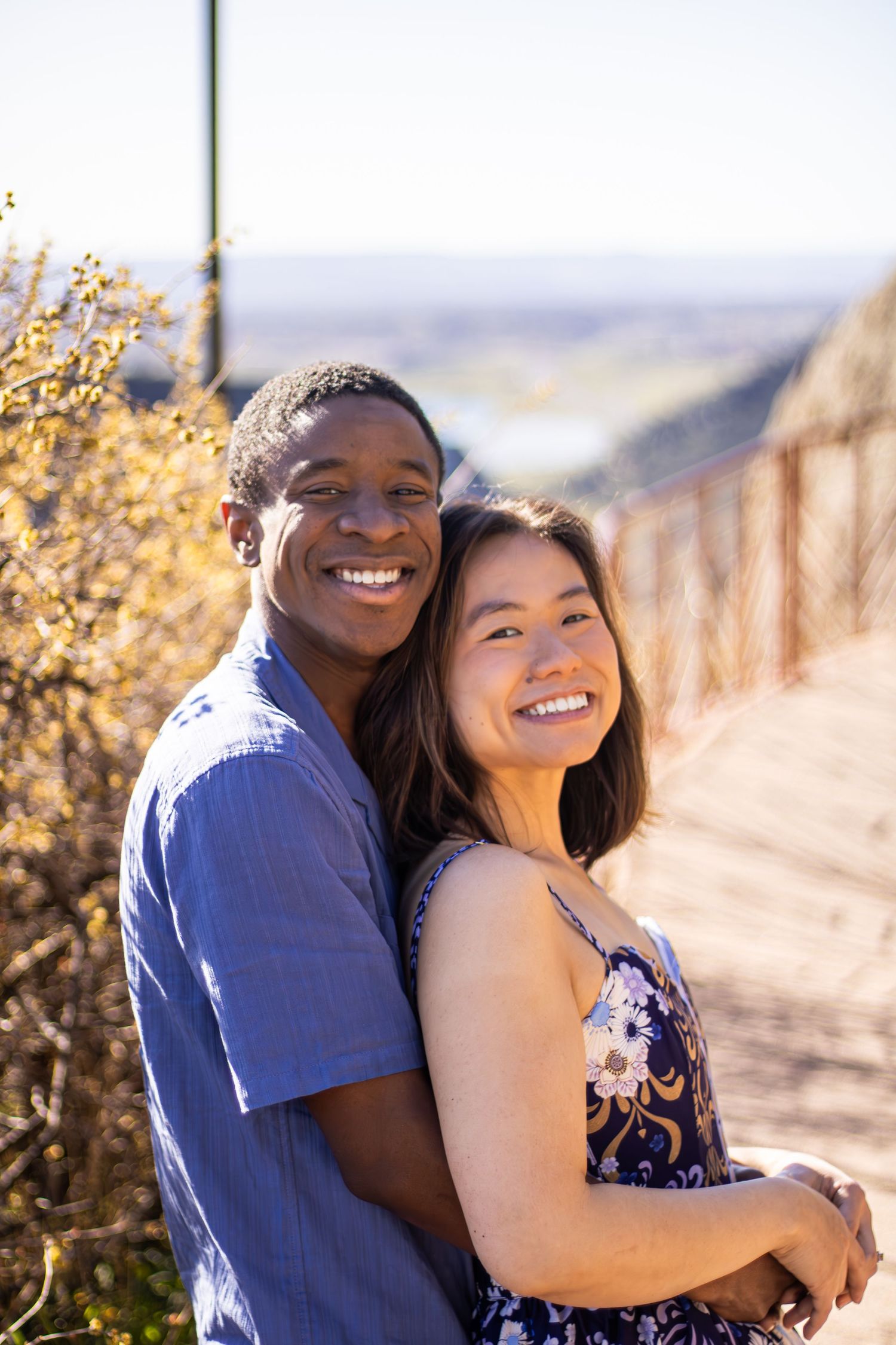 A joyful couple in coordinating blue outfits smiles and embraces on a scenic overlook.