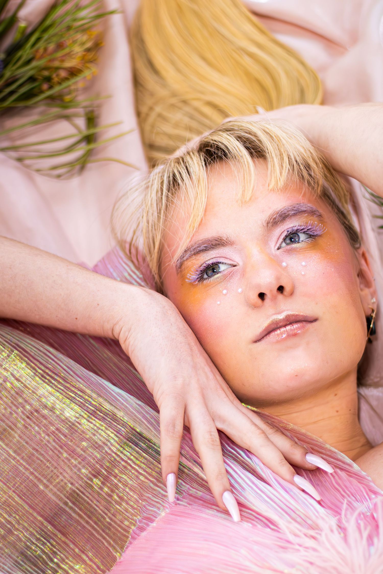 Close up artistic portrait with pink tones, dramatic lighting and plant elements creating ethereal mood.