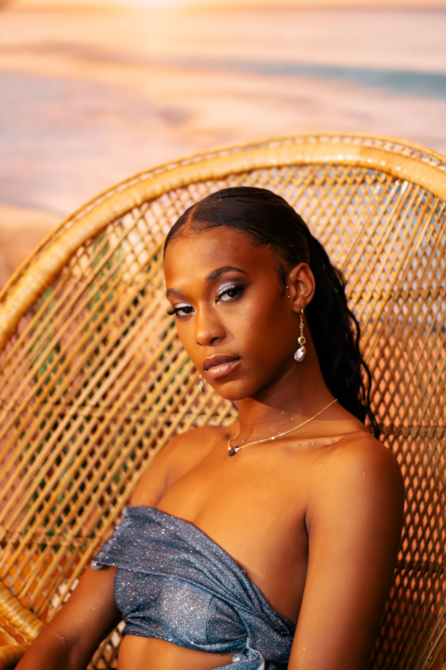 A portrait series showing a person in a blue dress seated on a wicker peacock chair at sunset.