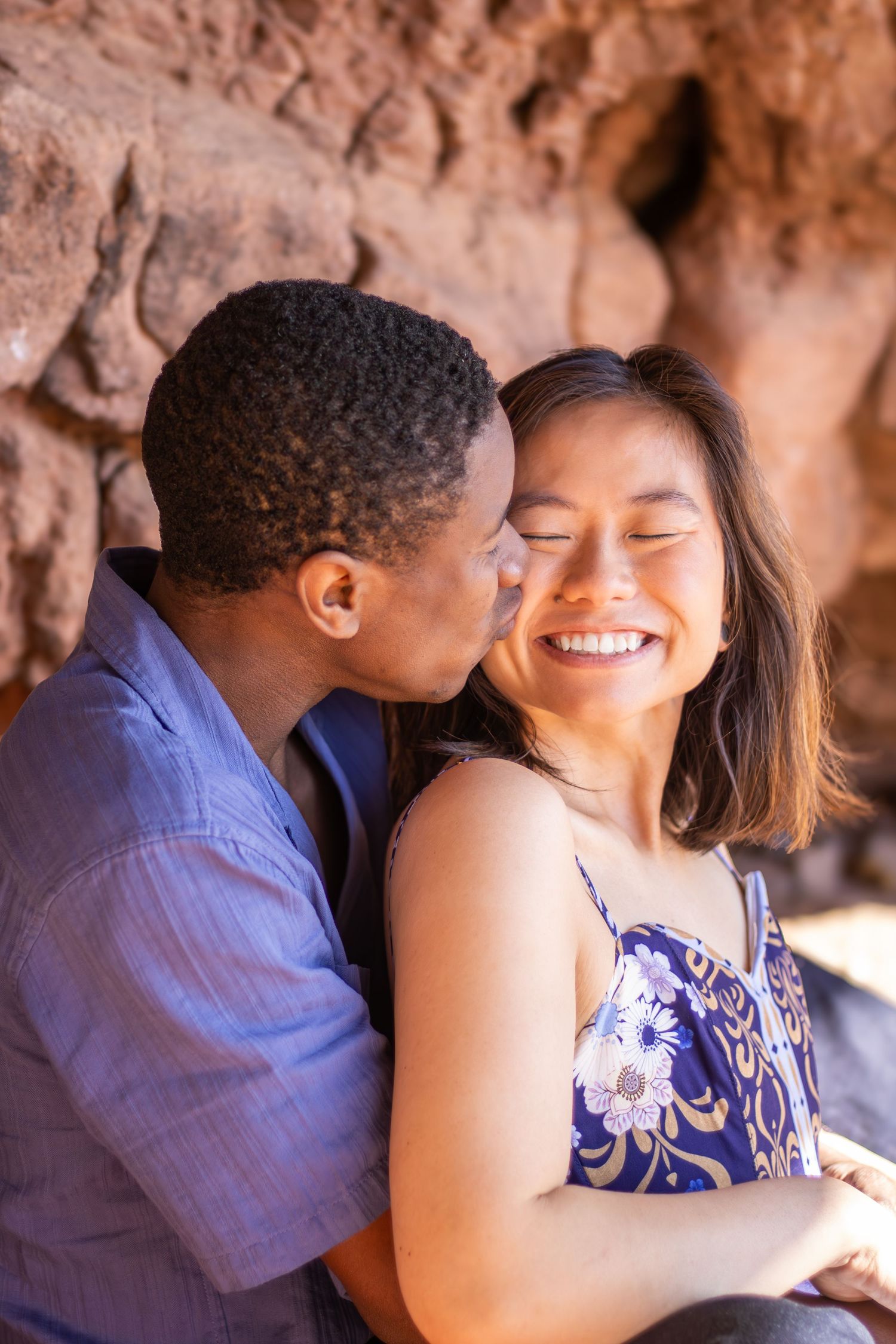 Two people share an intimate moment while sitting together against a rocky backdrop.