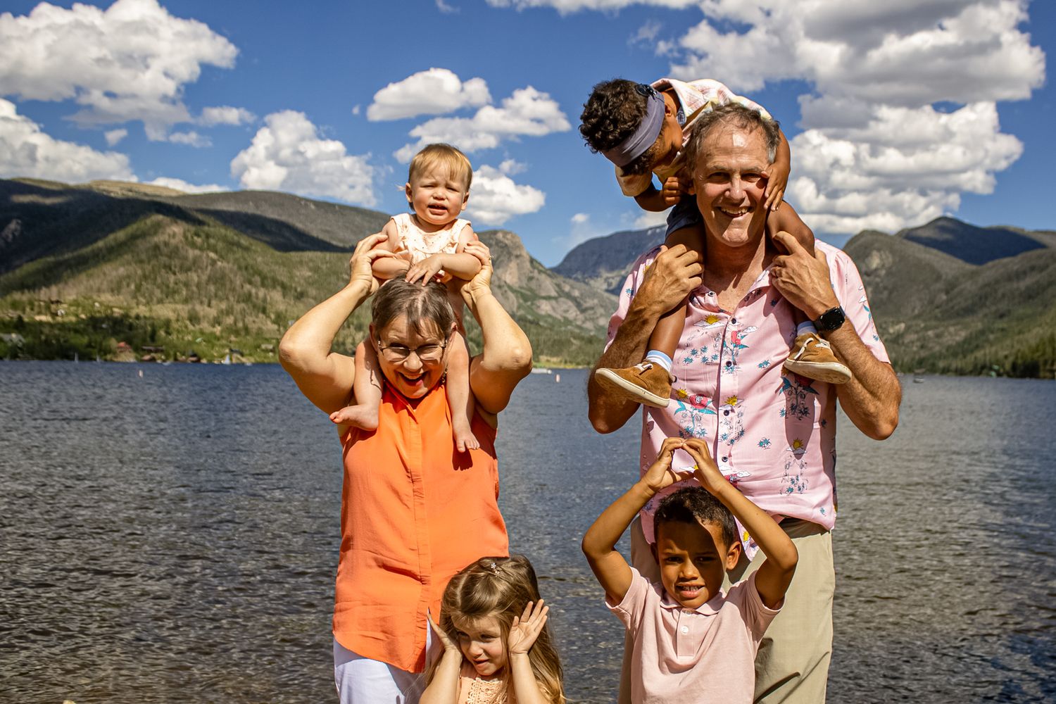 People having fun posing together on a sunny day near a mountain lake with blue skies and puffy clouds overhead.